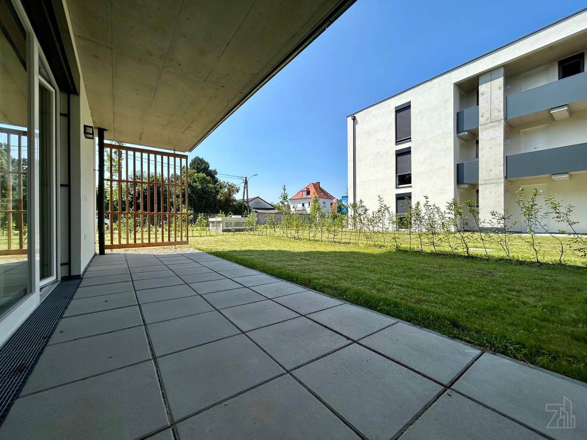 Geräumige gepflasterte Terrasse mit angrenzendem Rasenbereich und Blick auf die Umgebung.