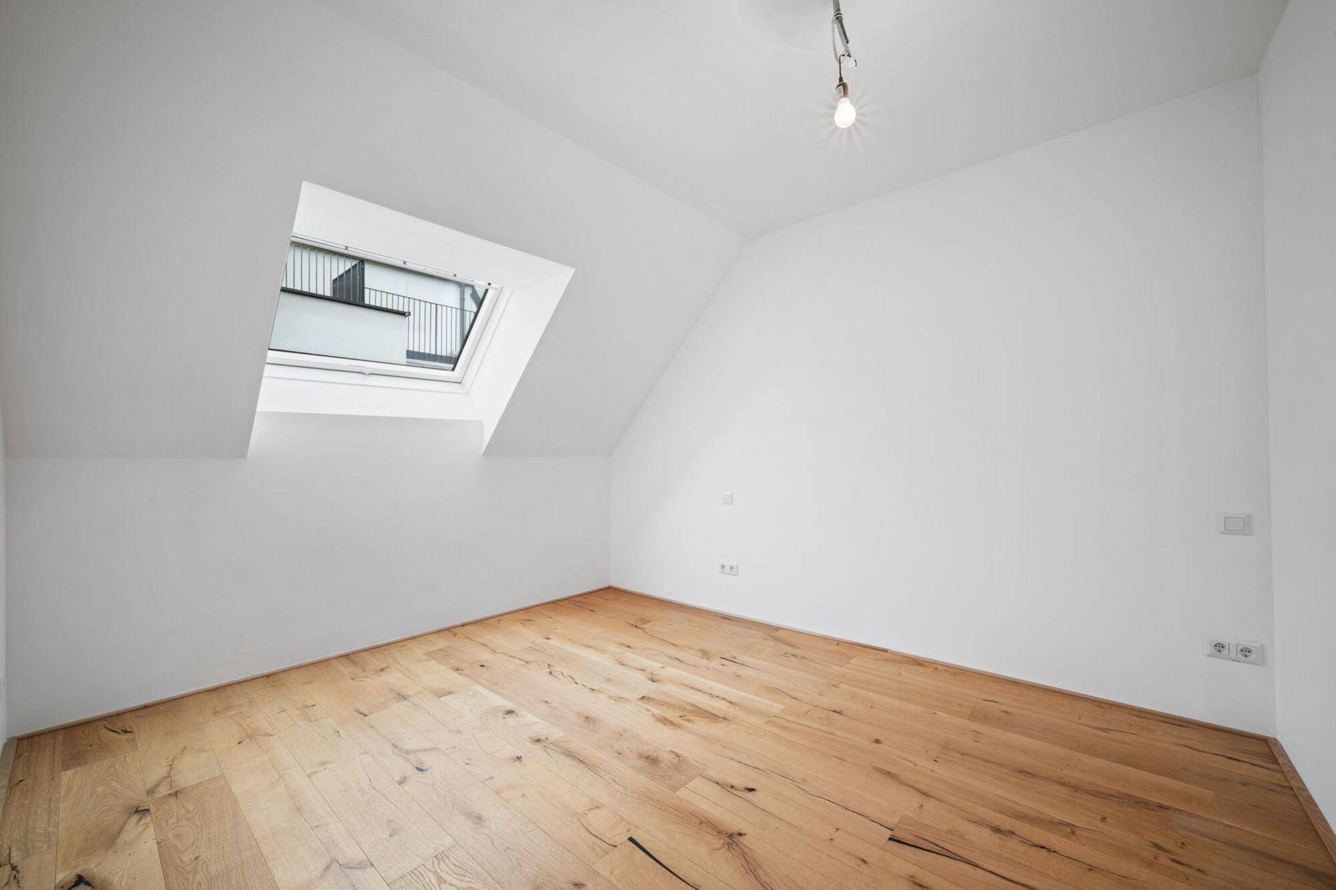 Helles Zimmer im Dachgeschoss mit Holzboden und Dachfenster für viel Licht.