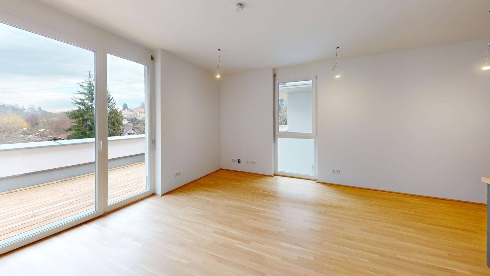 Heller Wohnraum mit Holzboden und Zugang zu einer großen Holzterrasse mit Weitblick.