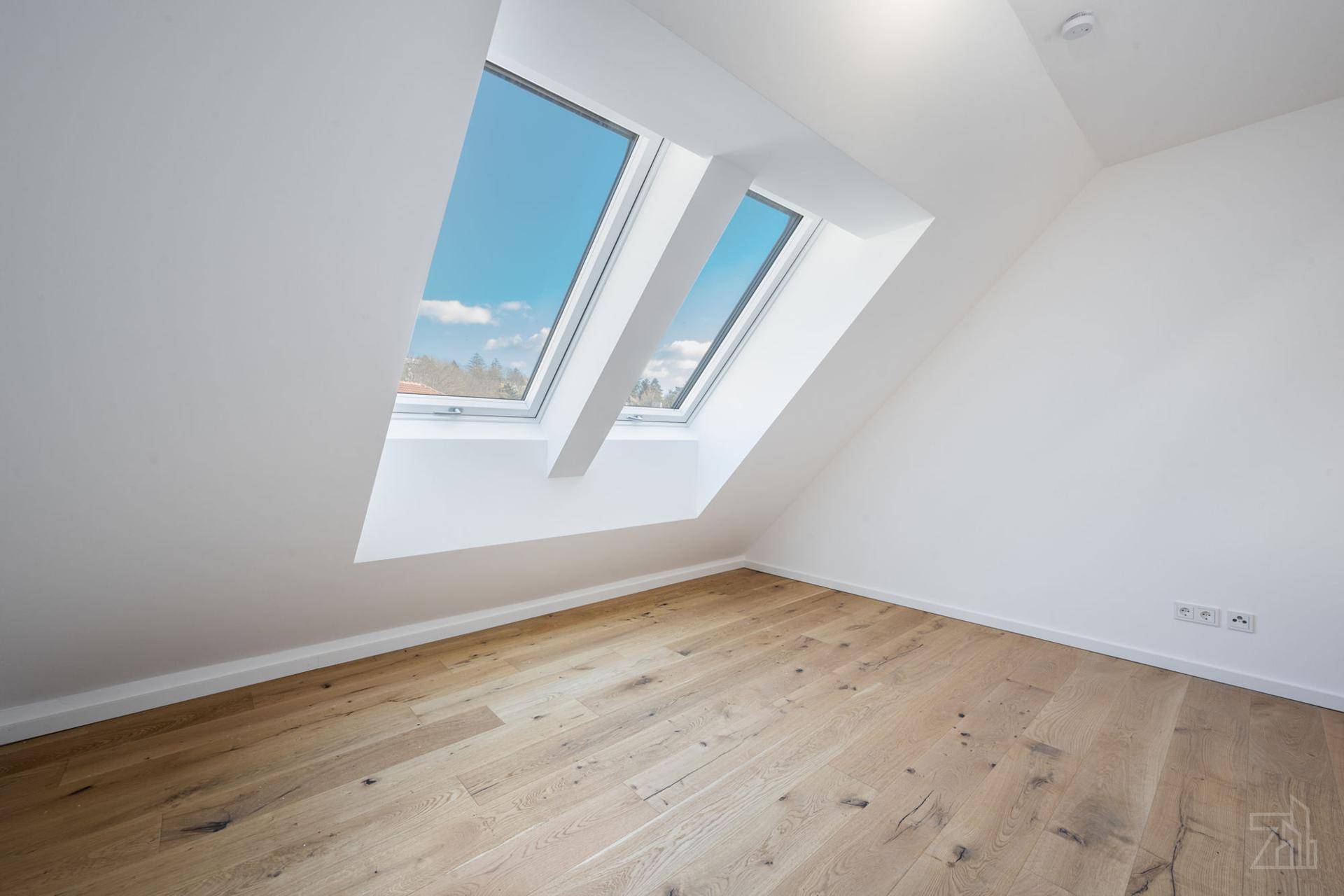 Heller Raum mit Holzboden, zwei Dachfenstern und schrägen Wänden im Dachgeschoss.