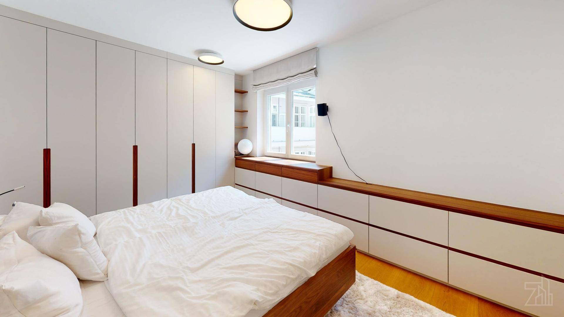 Schlafzimmer mit großem Bett, weißen Einbauschränken und Holzablage unter dem Fenster.