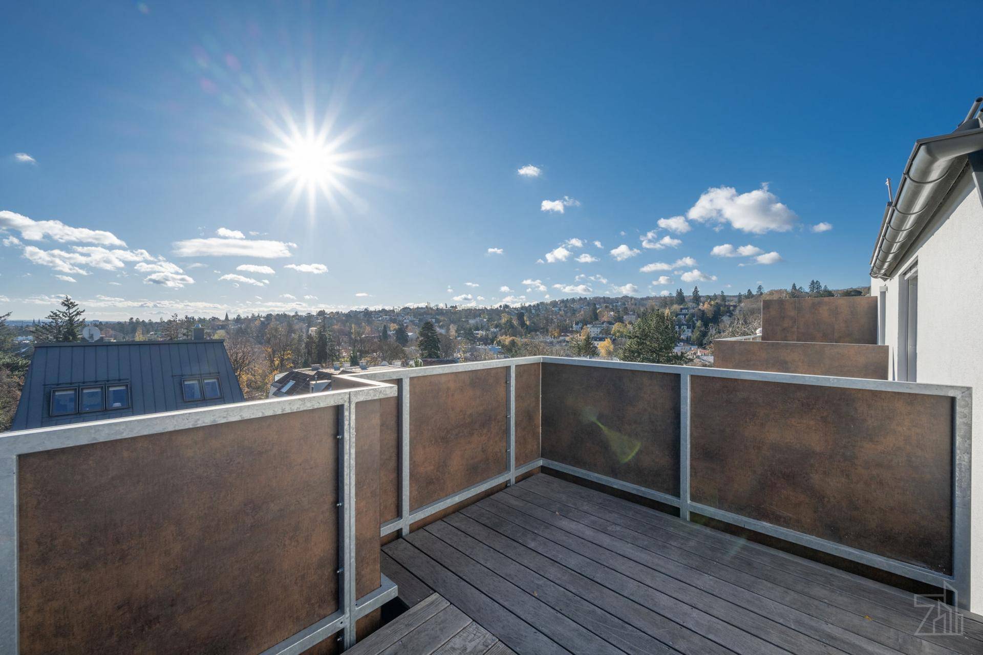 Sonniger Balkon mit Holzboden, modernem Geländer und weitem Blick über die Stadt.