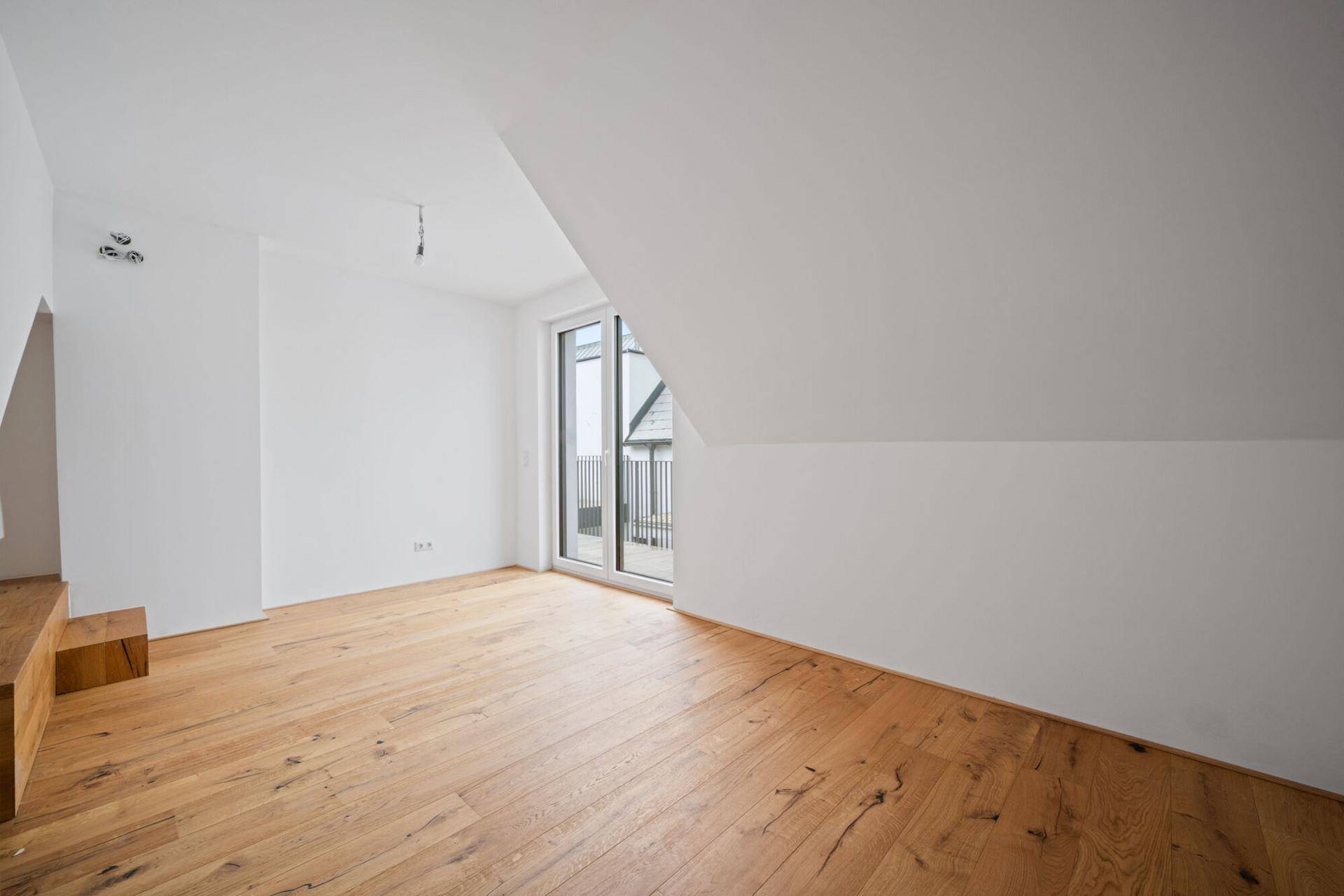 Dachgeschosszimmer mit Holzboden, schrägen Wänden und Zugang zu einem Balkon.