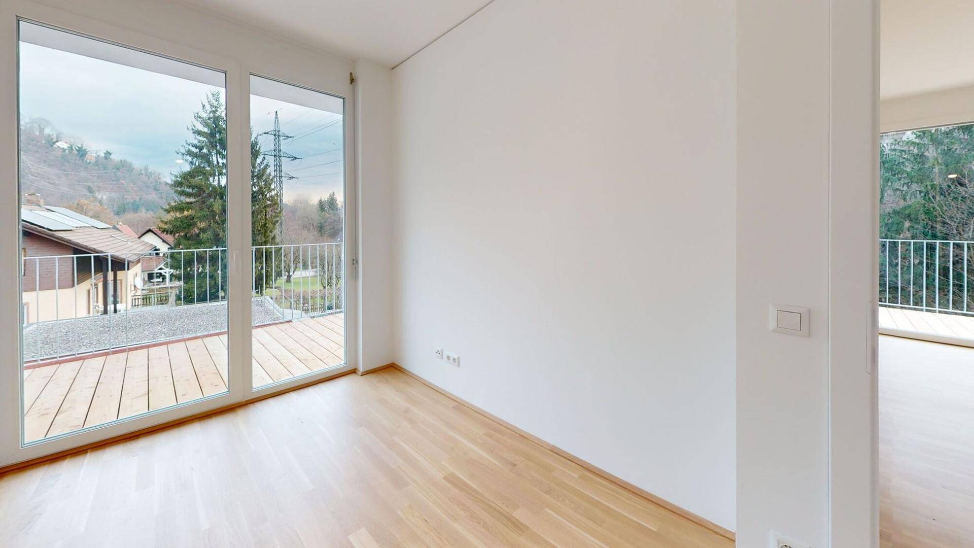 Heller Wohnraum mit Holzboden und raumhohen Fenstern, die einen weiten Blick ermöglichen.