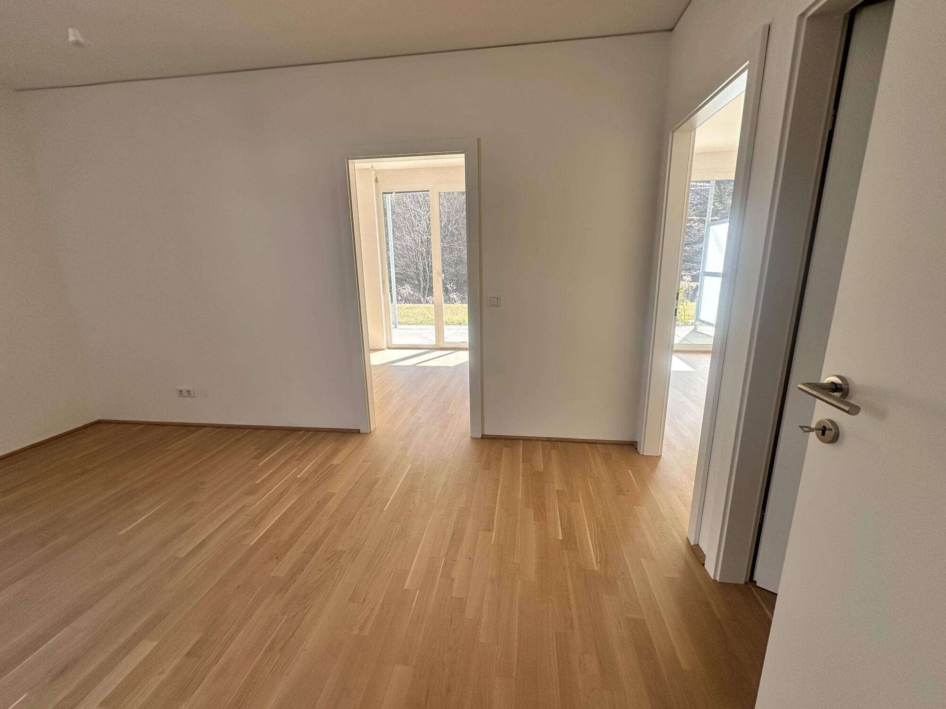 Leerer Flur mit hellem Holzparkettboden und offenen Türen, die zu weiteren hellen Räumen führen.