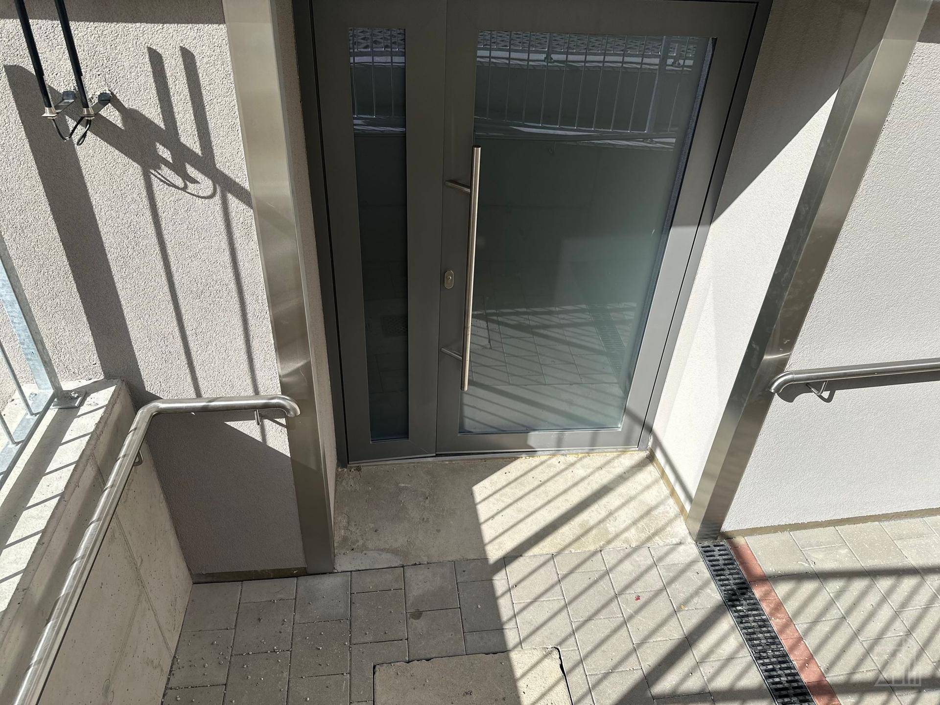 Eingangstür zu einem Gebäude mit Glaspaneelen und seitlichen Handläufen.