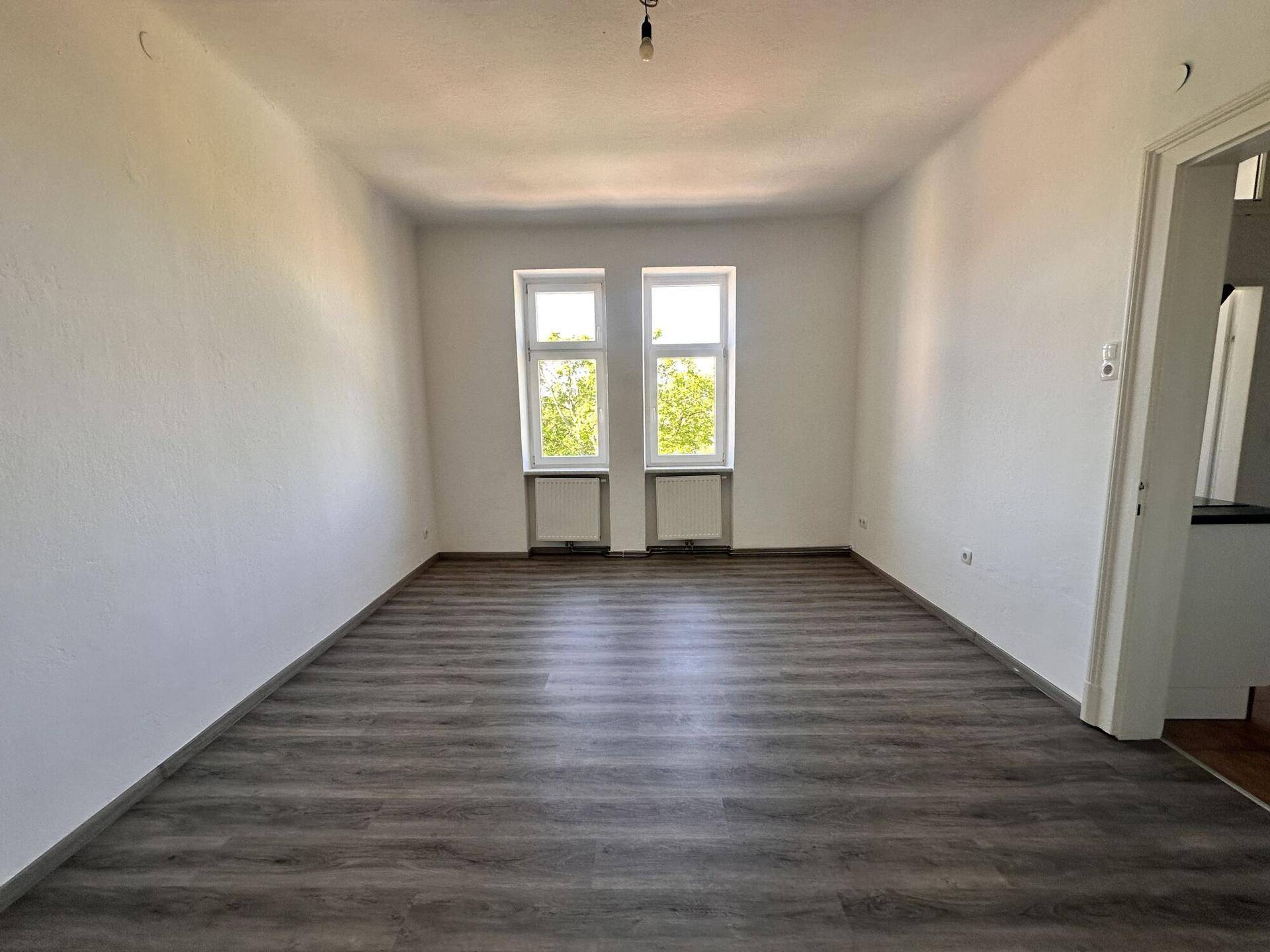 Heller Raum mit grauem Laminatboden und weißen Wänden, bereit zur Einrichtung.