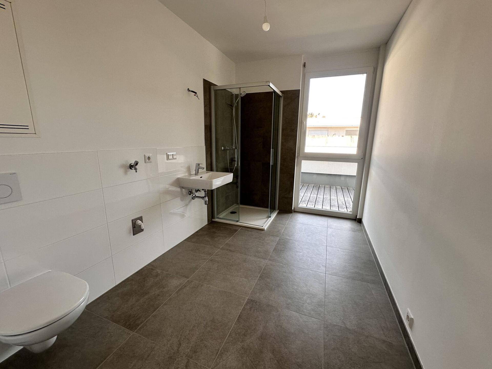 Modernes Badezimmer mit Dusche, WC und Waschbecken, ausgestattet mit großen, dunklen Fliesen.