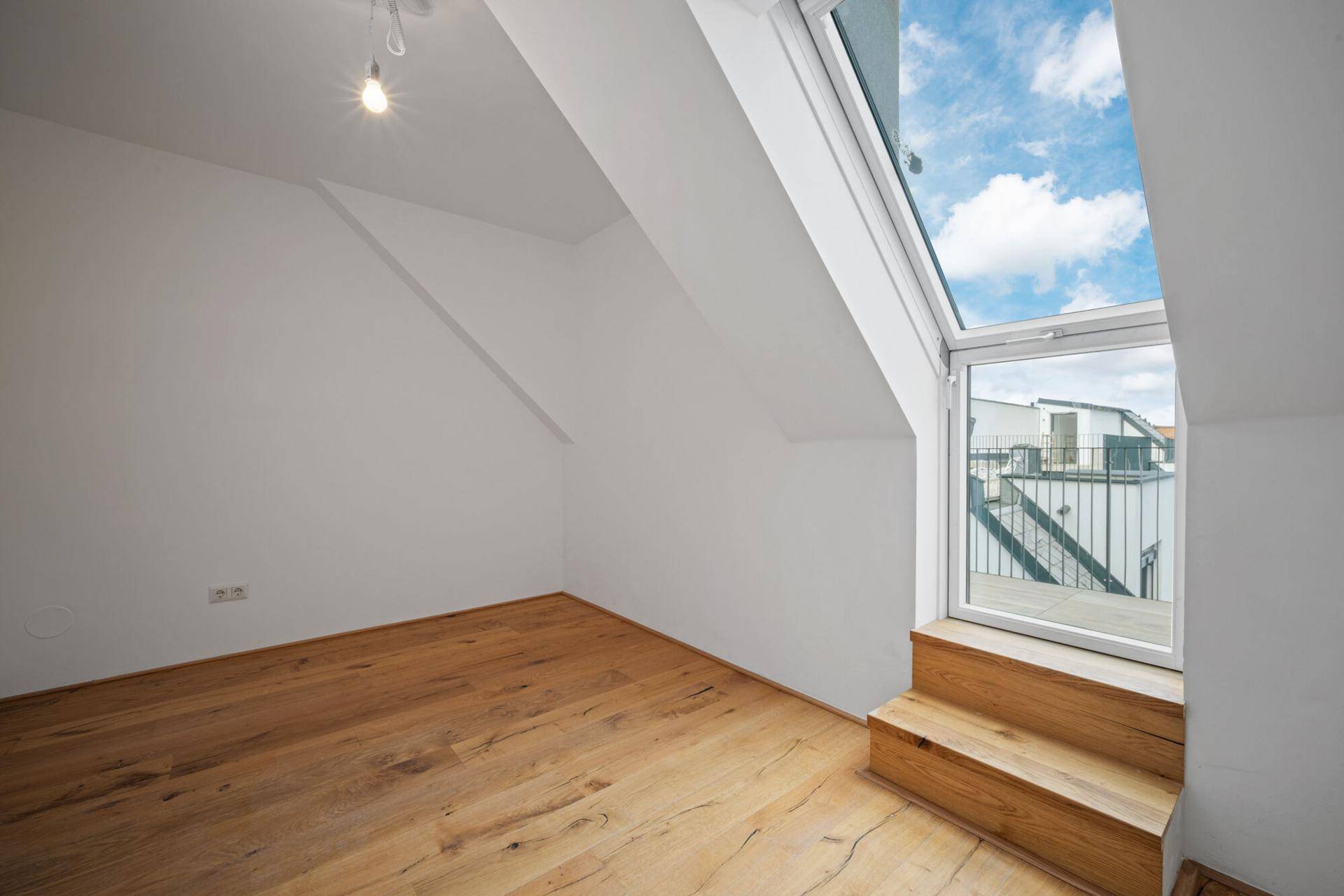 Kleines, helles Zimmer im Dachgeschoss mit Holzboden und einem großen Dachfenster mit Ausblick.