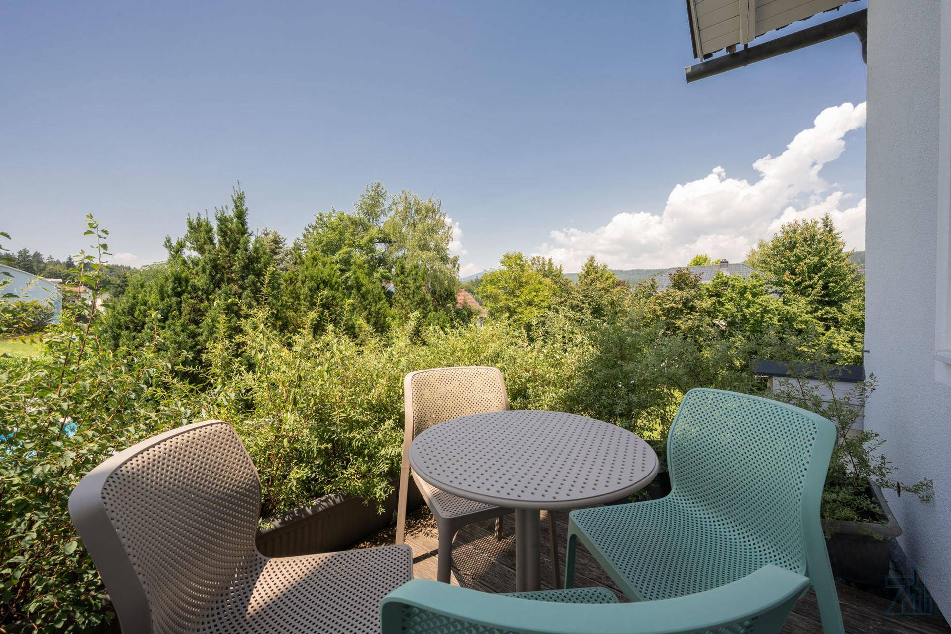 Kleiner Balkon mit Sitzgelegenheiten und Blick auf grüne Bäume und die Umgebung.