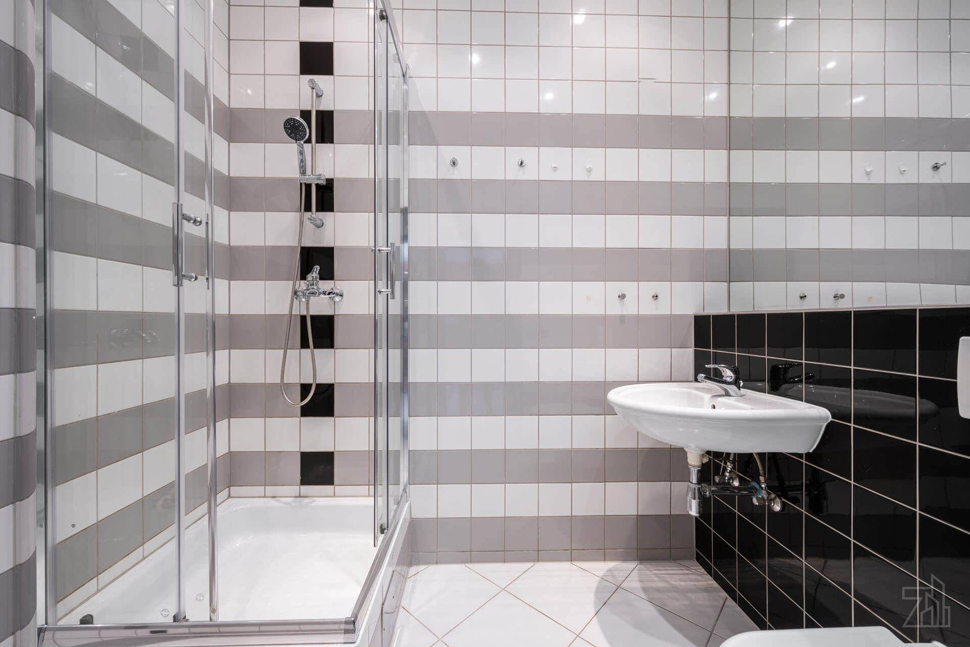 Modernes Badezimmer mit gestreiften Wandfliesen, Duschkabine und wandmontiertem Waschbecken.