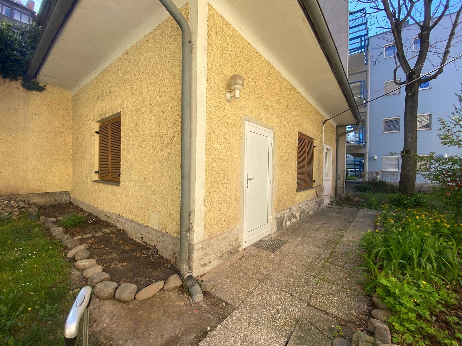 Seitlicher Gartenbereich mit gepflastertem Weg und einem Nebengebäude.