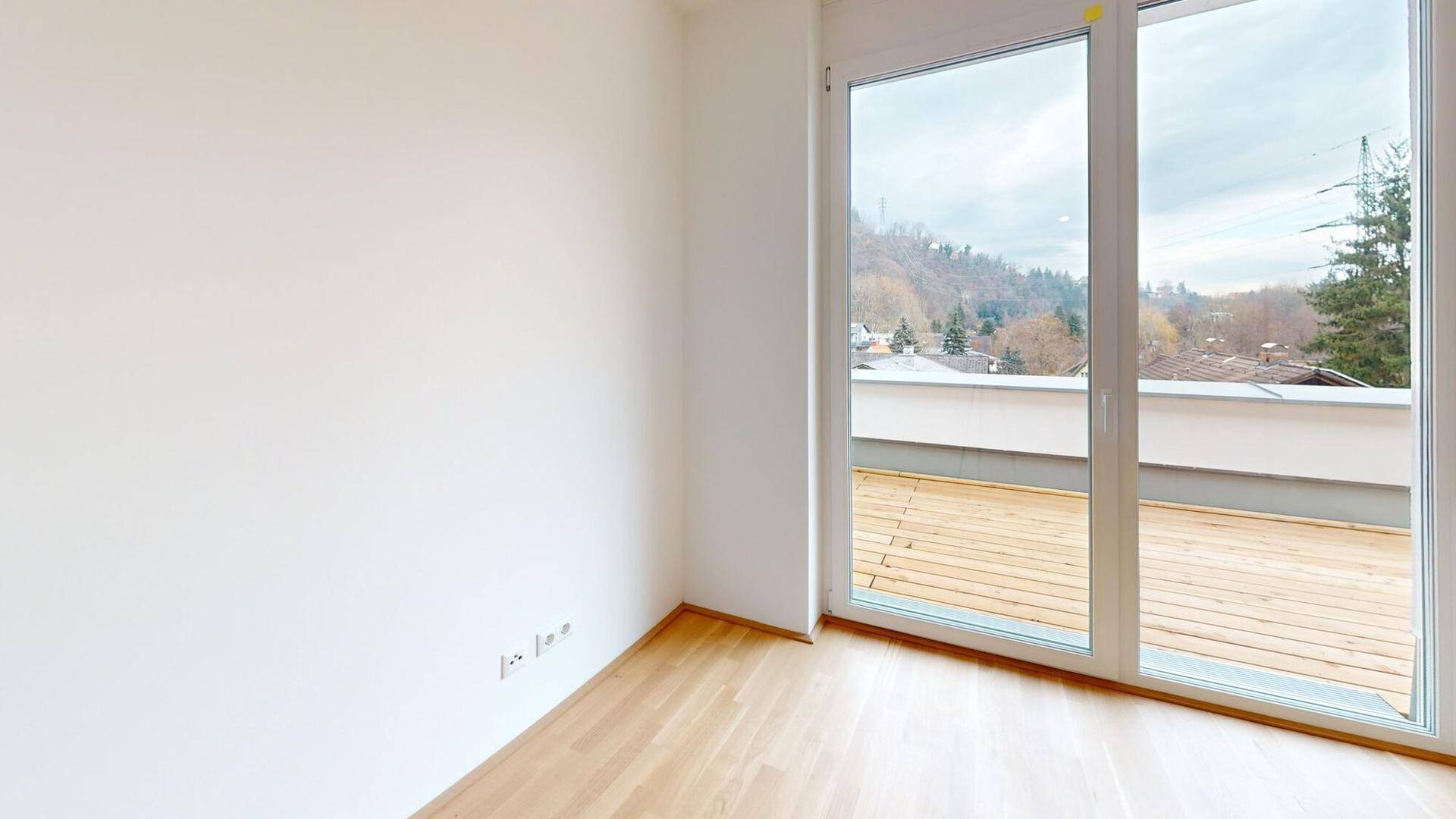 Lichtdurchflutetes Zimmer mit Holzboden und großem Fenster zur Terrasse.