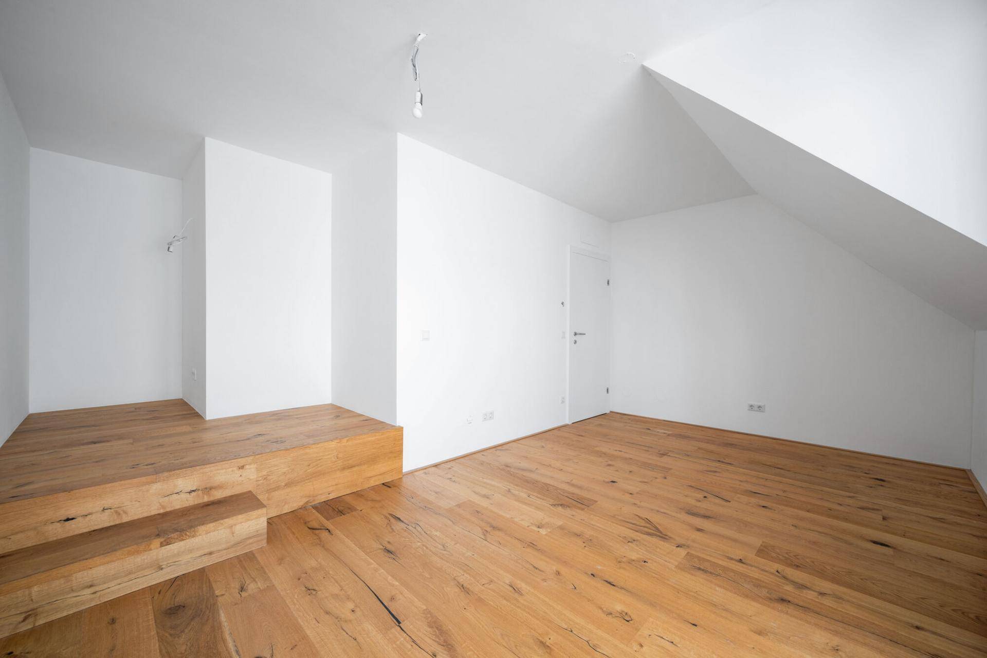 Heller Raum mit Holzboden, Dachschräge und einer erhöhten Holzplattform.