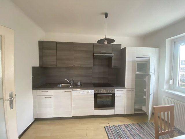 Helle Einbauküche mit Holzoptik-Schränken, integriertem Kühlschrank und Fenster.