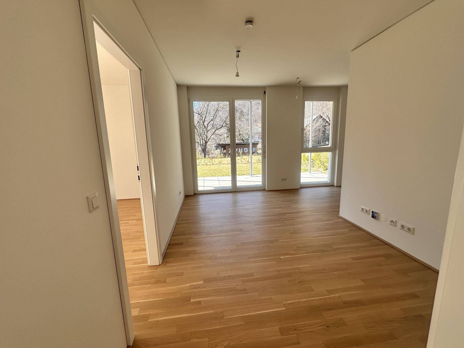 Geräumiger, heller Raum mit Holzboden und mehreren Fenstern zum Garten.