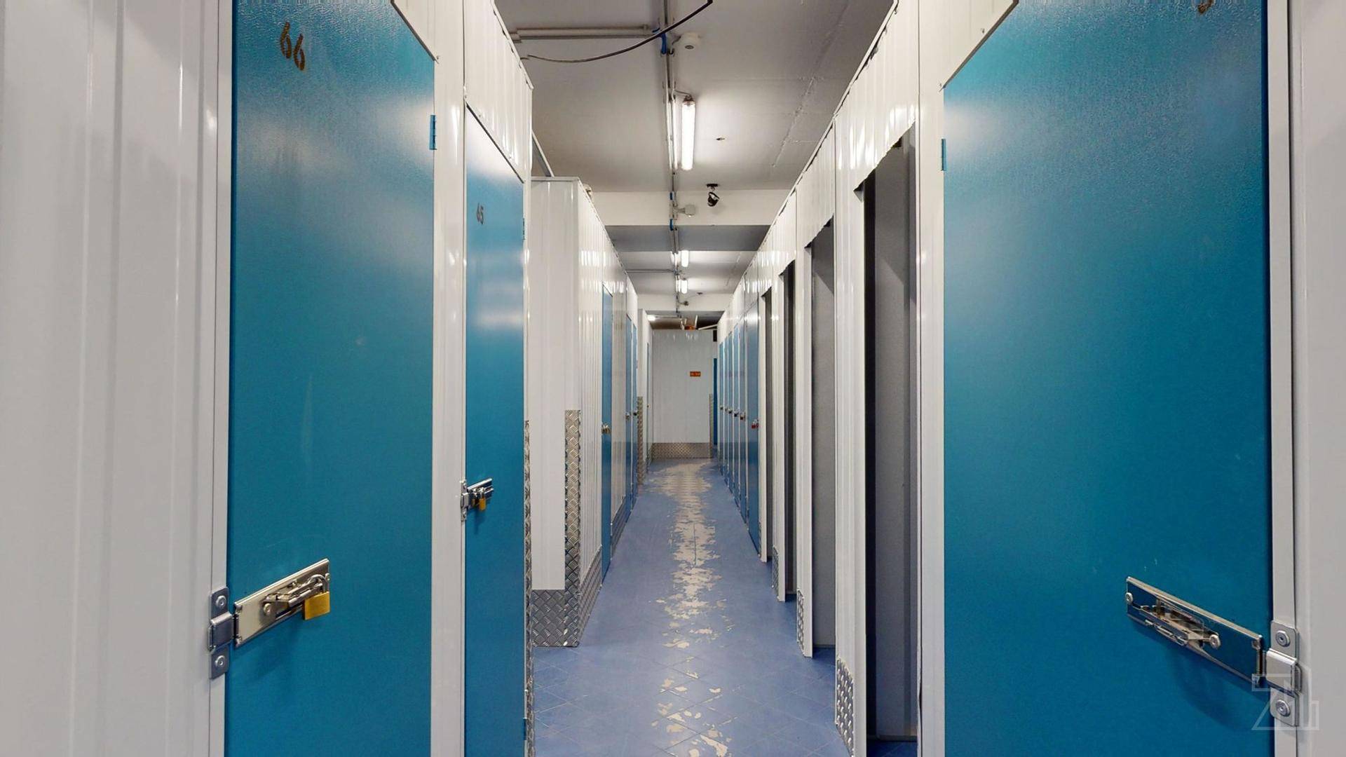 Weiterer Gang in einem Lagerraum mit vielen blauen Türen und hellen, weißen Wänden.