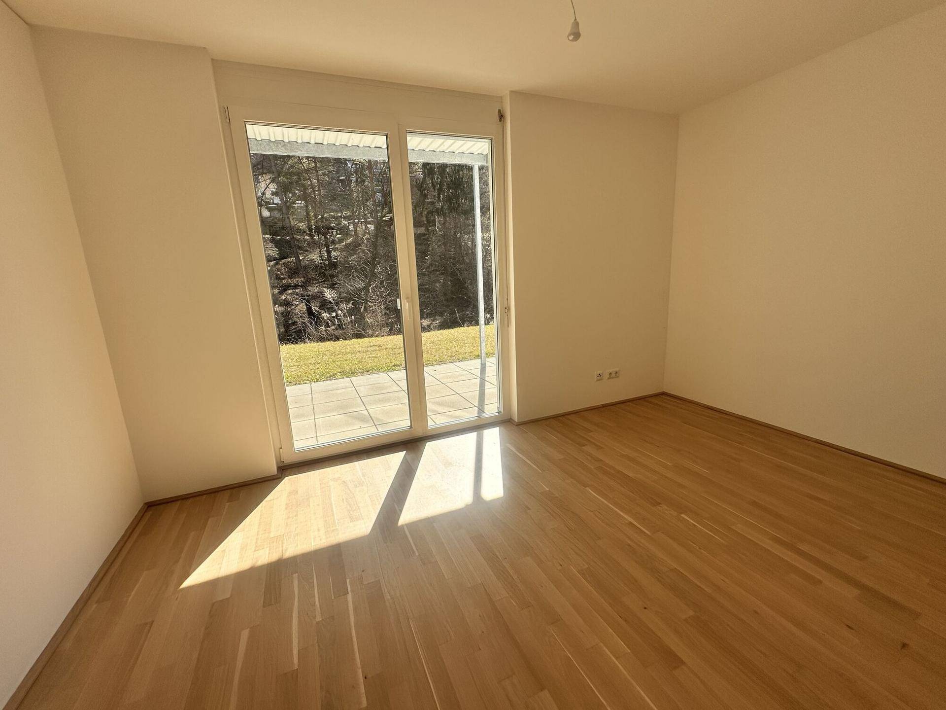Sonniger Raum mit Holzboden und direktem Zugang zur Terrasse und zum Garten.