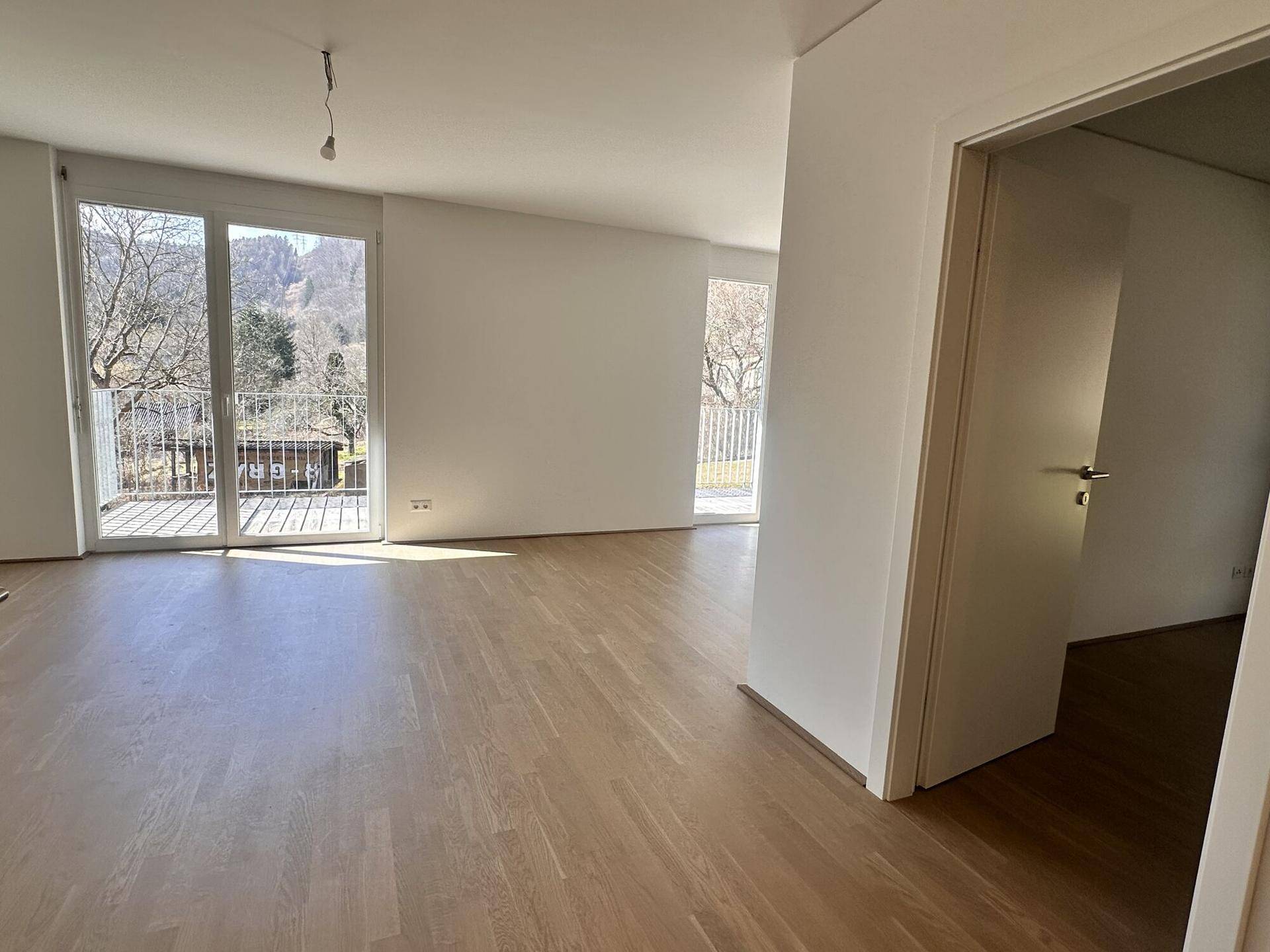 Lichtdurchfluteter Wohnbereich mit Holzboden und Zugang zu einem weiteren Raum.