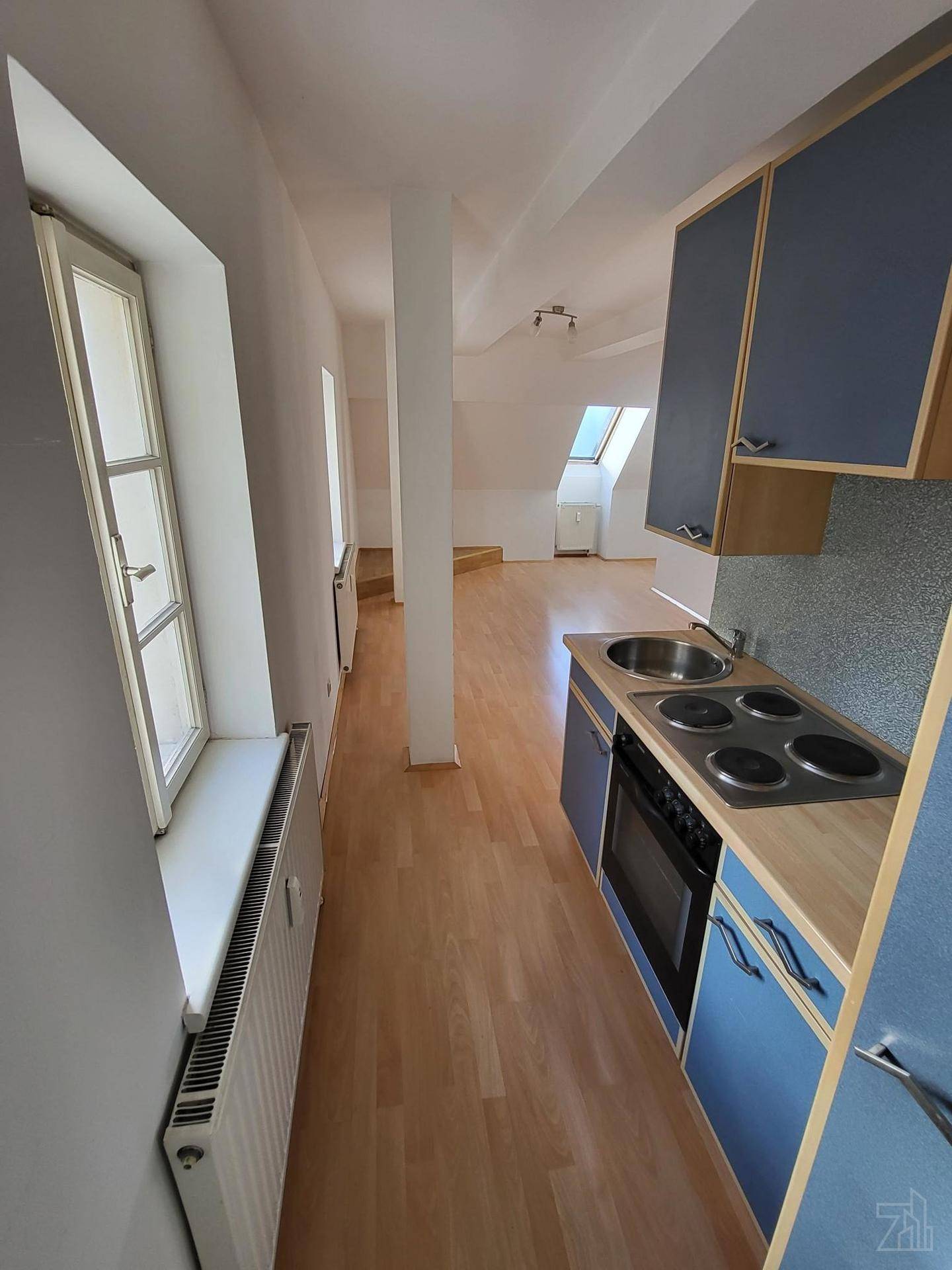Kleine Küchenzeile im Dachgeschoss mit blauen Schränken und Kochfeld.