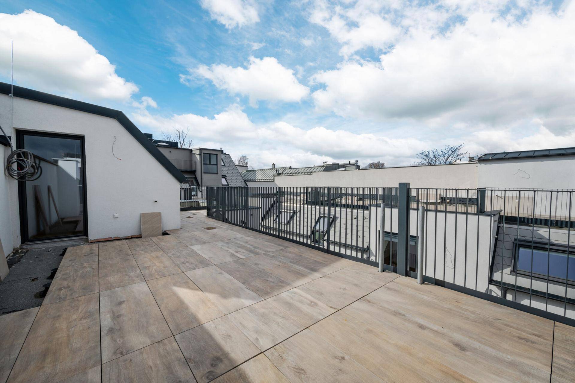 Große Dachterrasse mit Fliesenboden und Metallgeländer unter blauem Himmel.