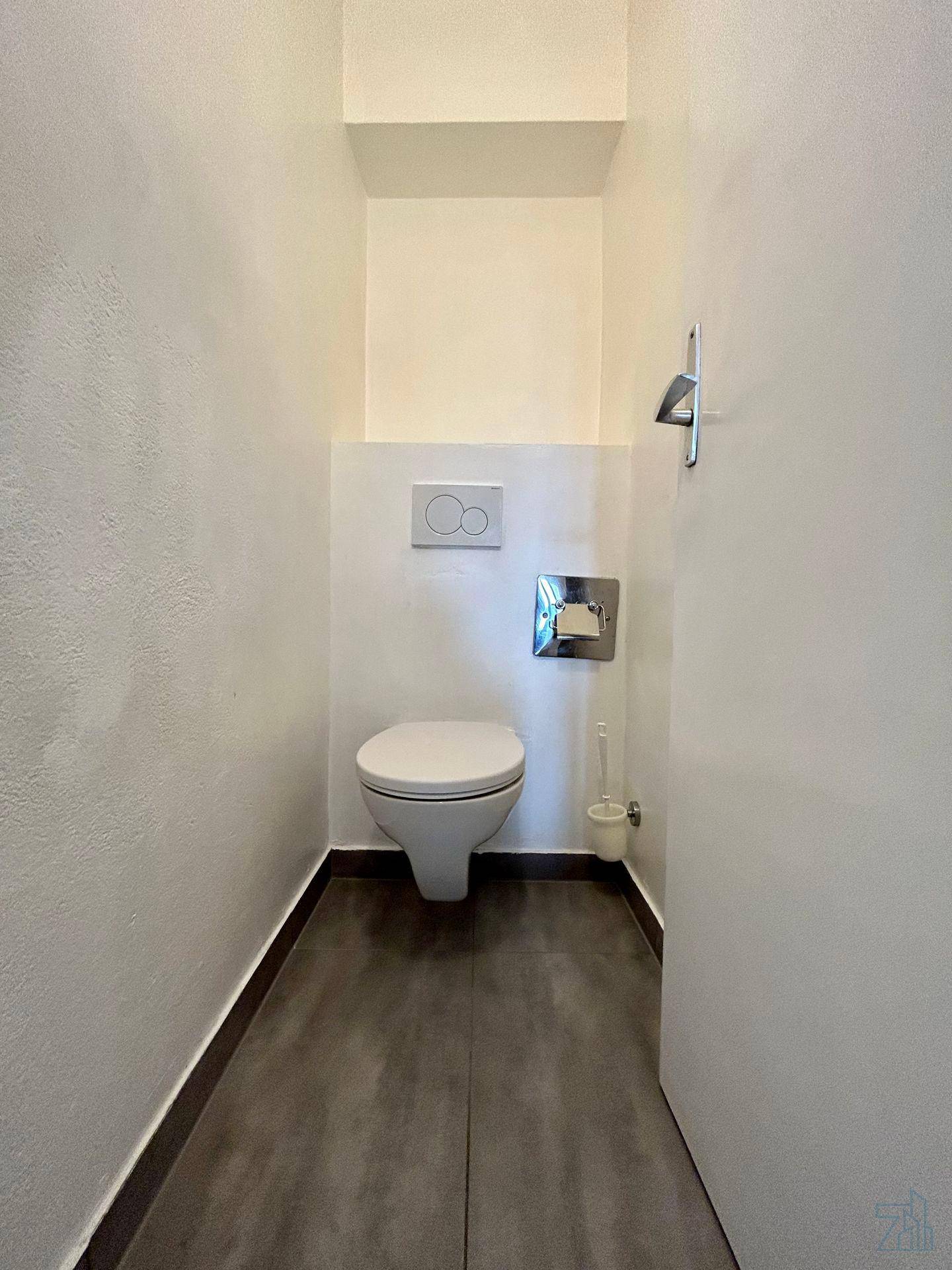 Kleines, funktionales WC mit wandhängender Toilette und dunklen Bodenfliesen.