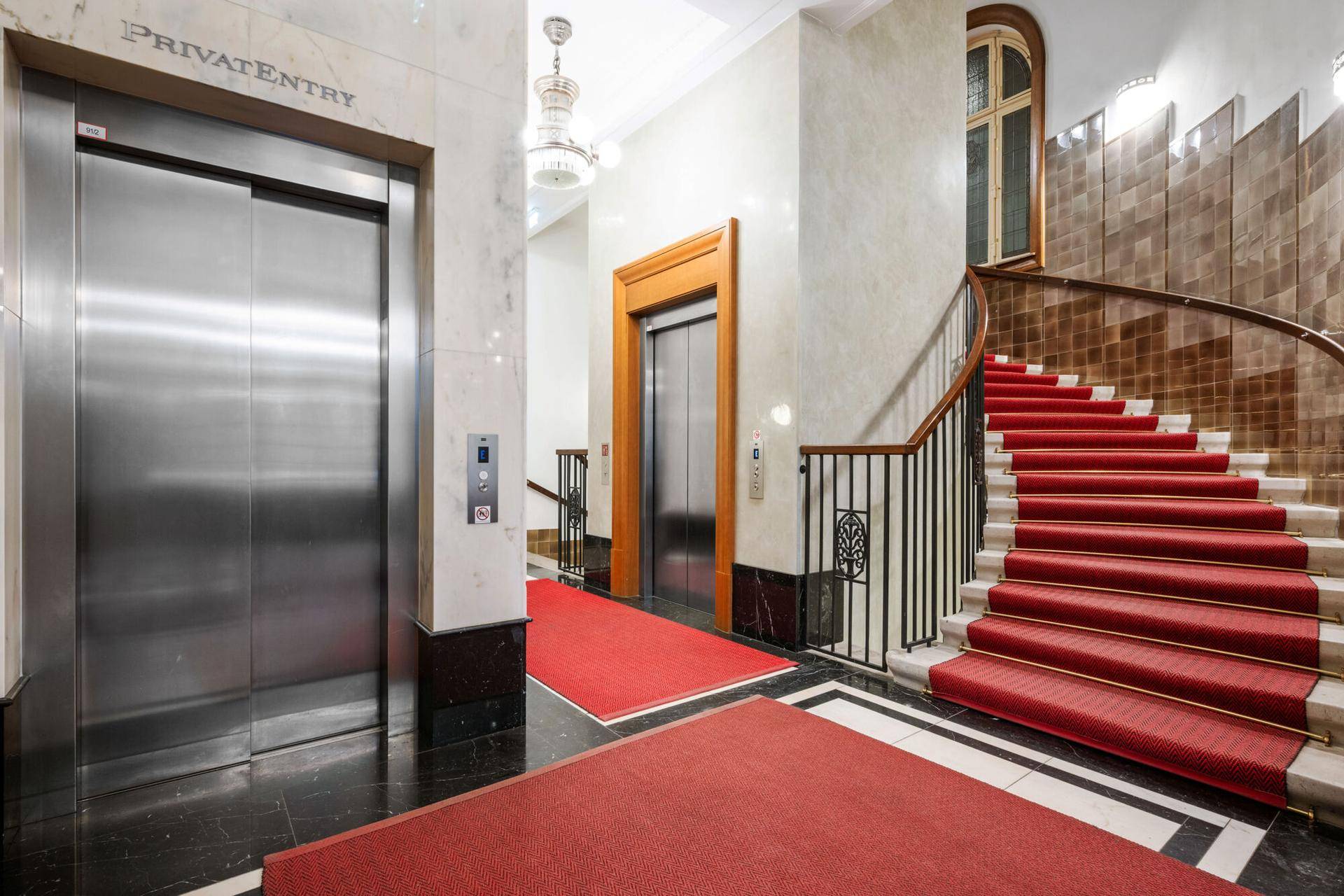 Prächtiges Entrée mit rotem Teppich, geschwungener Treppe und zwei Aufzügen.