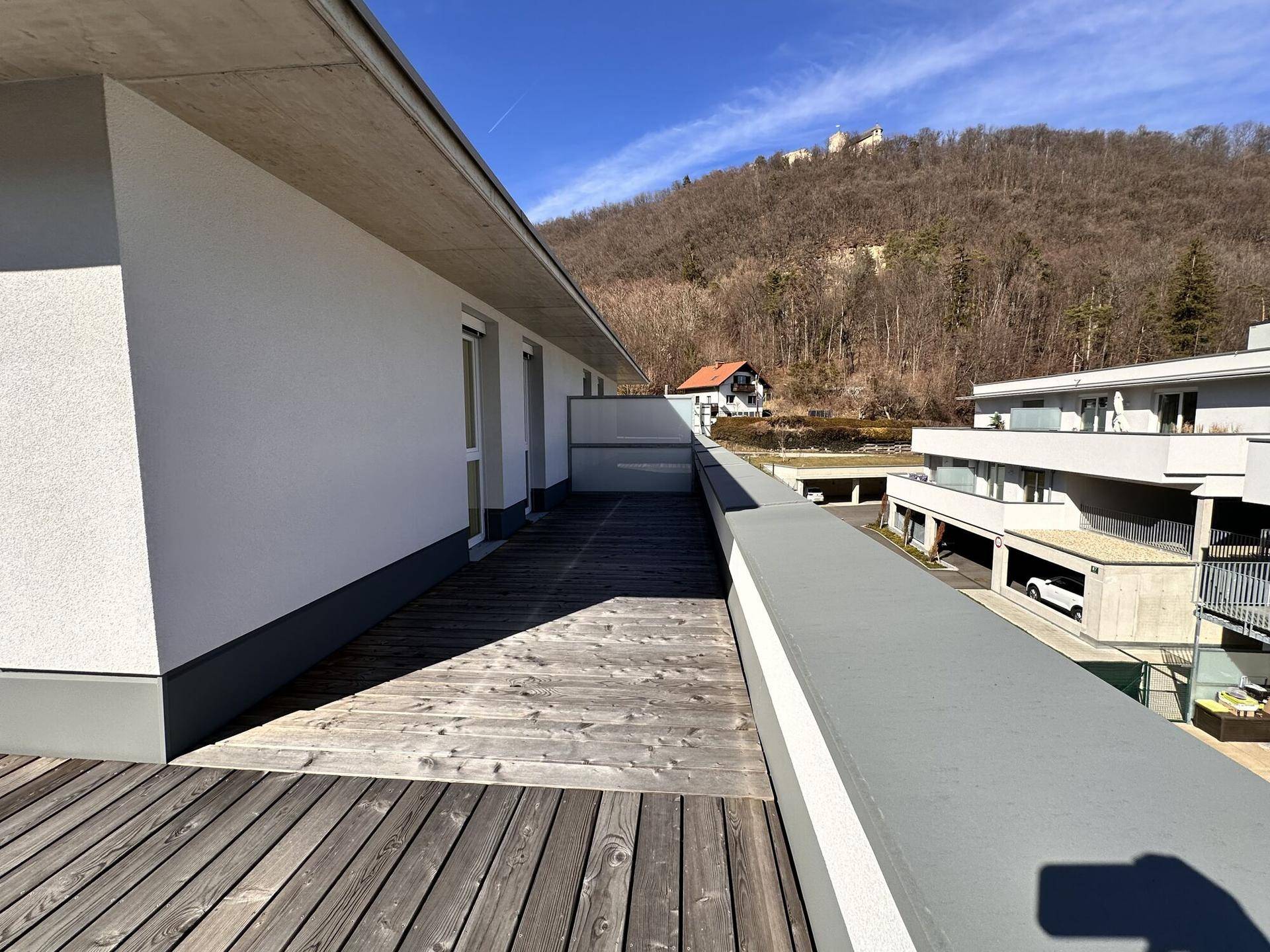 Lange Dachterrasse mit Holzdielen und Blick auf die bewaldeten Hügel und die Nachbargebäude.