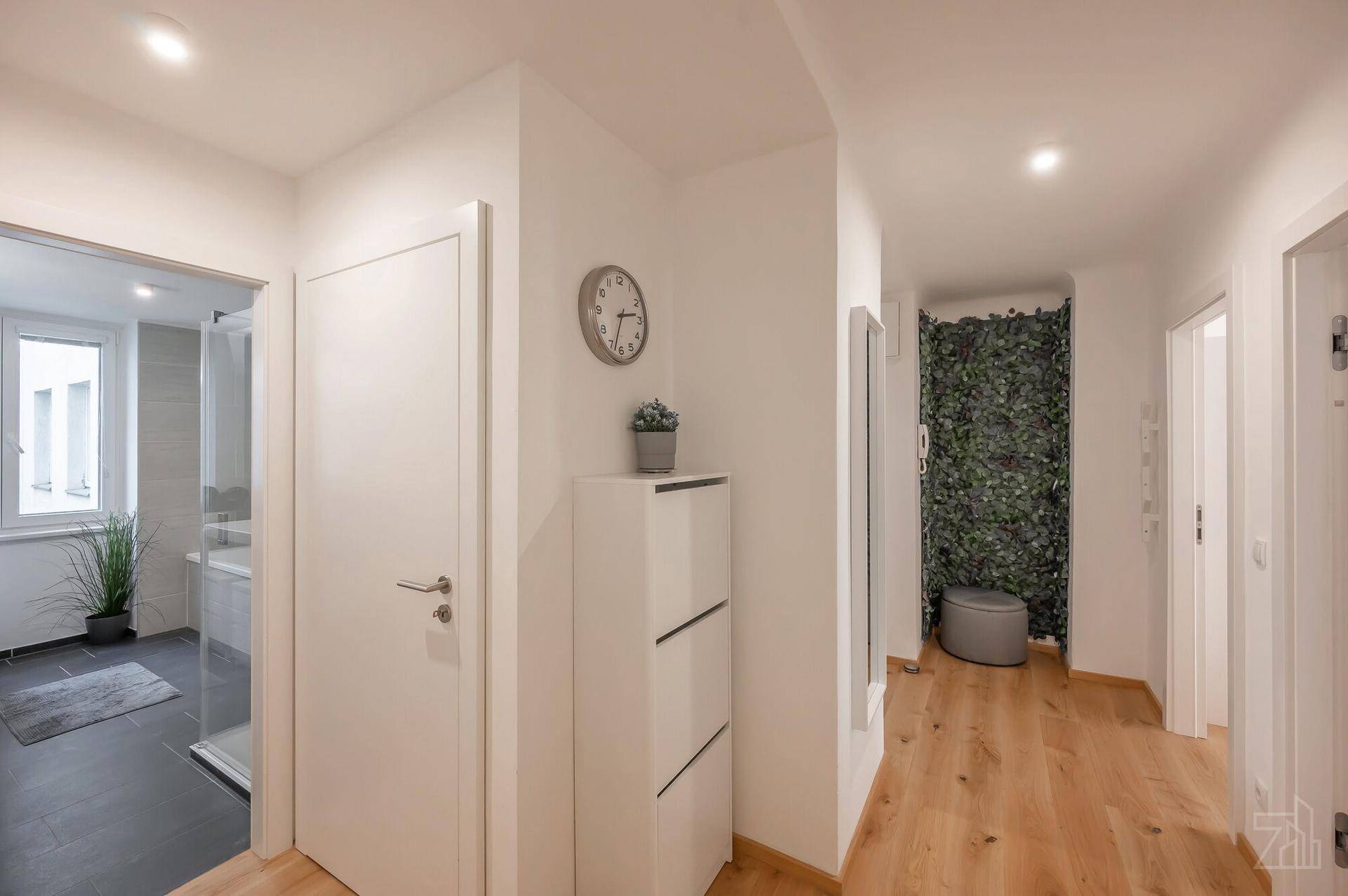 Moderner Flur mit Schuhschrank, Spiegel und Zugang zu einem Badezimmer mit Dusche.