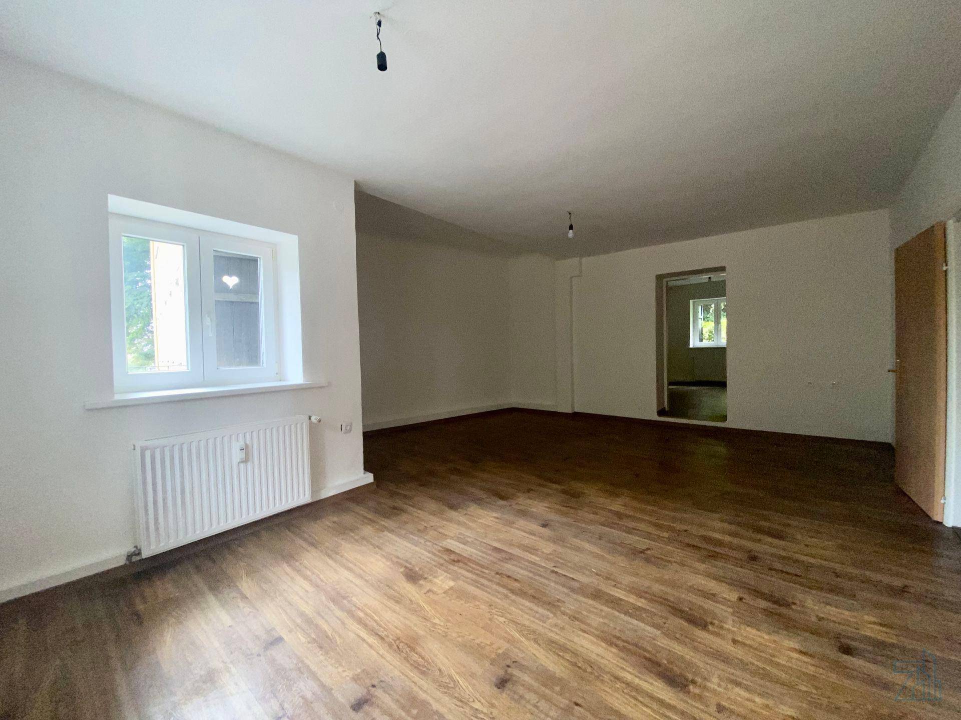 Heller Wohnraum mit Holzboden und großem Fenster, der viel Tageslicht hereinlässt.