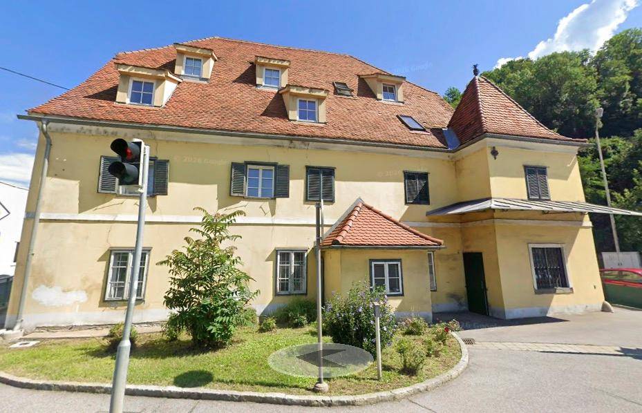 Gelbes Gebäude mit rotem Ziegeldach und Gaubenfenstern an einer Straße.
