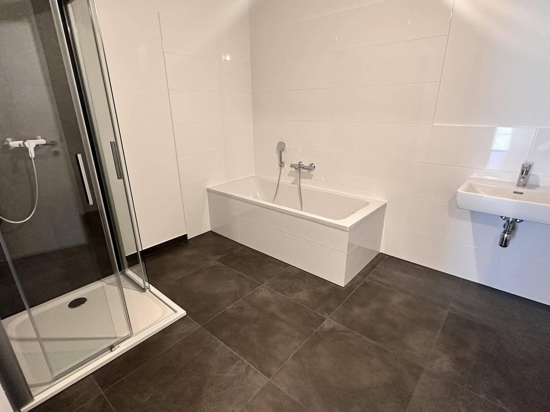 Modernes Badezimmer mit dunklen Fliesen, Badewanne, Duschkabine und Waschbecken.
