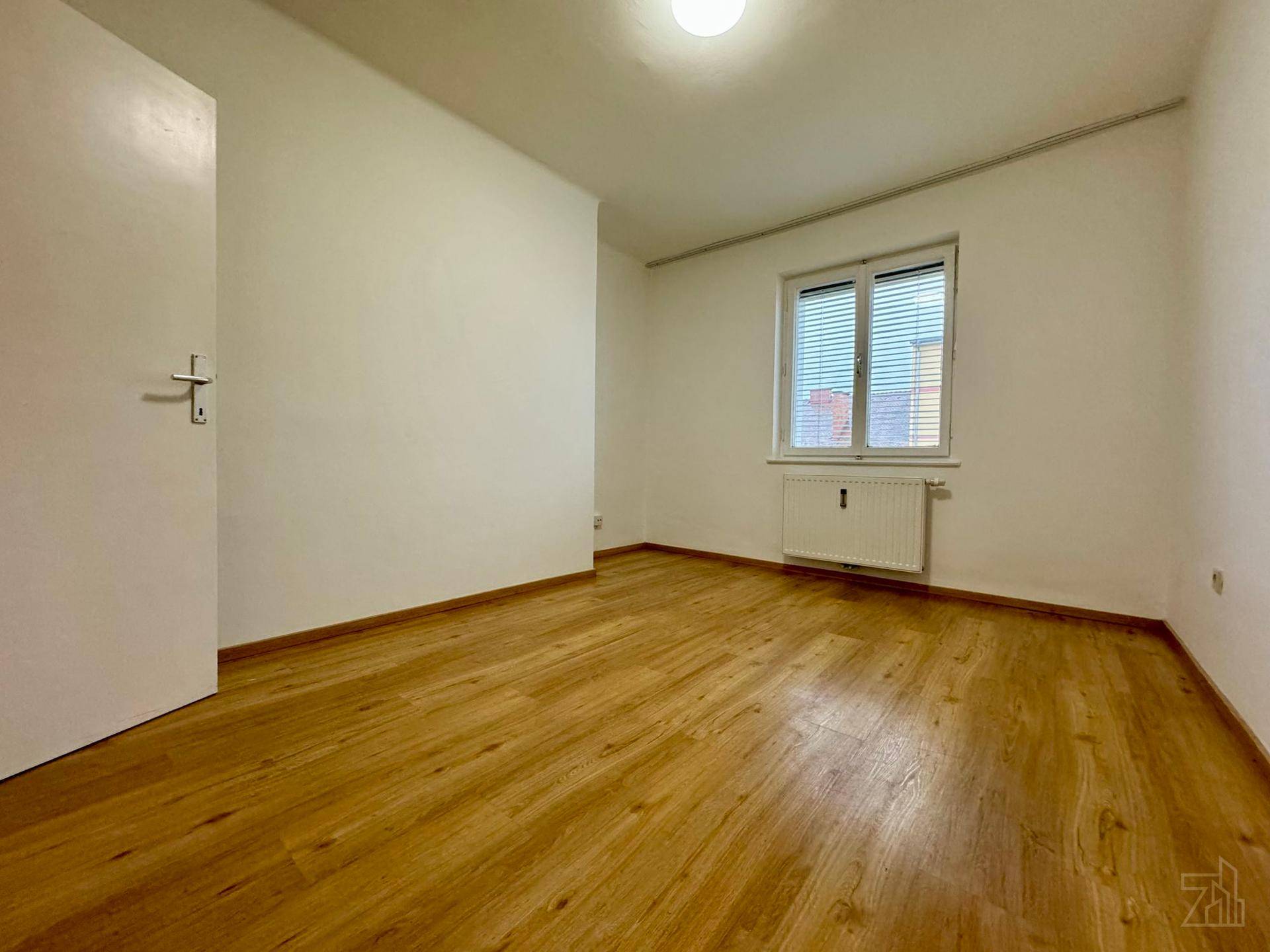 Schlafzimmer mit Laminatboden, weißen Wänden und Fenster mit Jalousien.