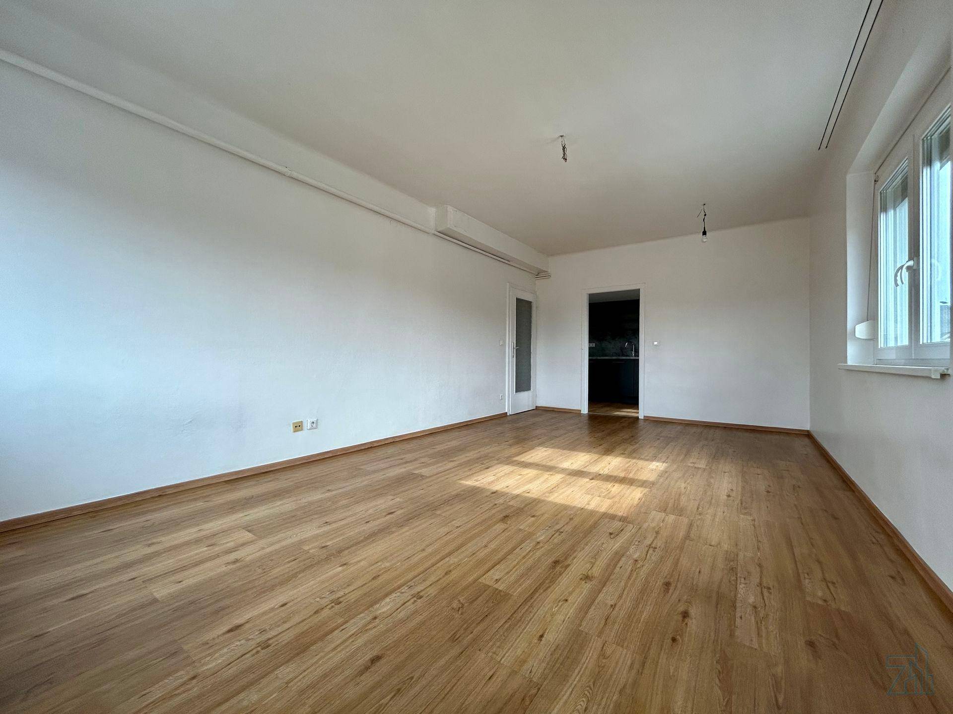 Geräumiger, heller Raum mit Holzboden und Fenstern, ideal für Wohn- oder Schlafzimmernutzung.