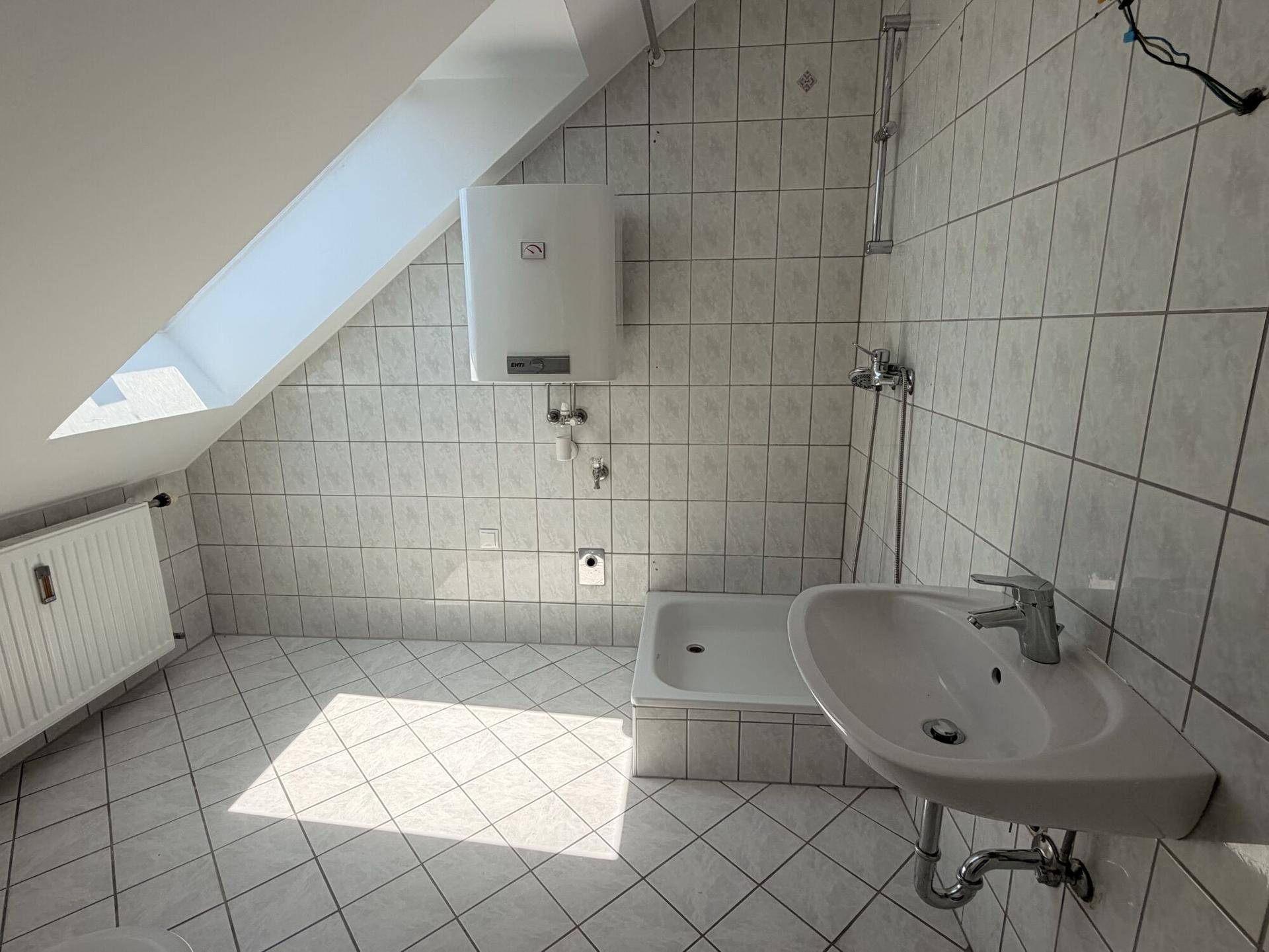 Helles Badezimmer mit Fliesen, Dusche, Waschbecken und Dachfenster in der Schräge.