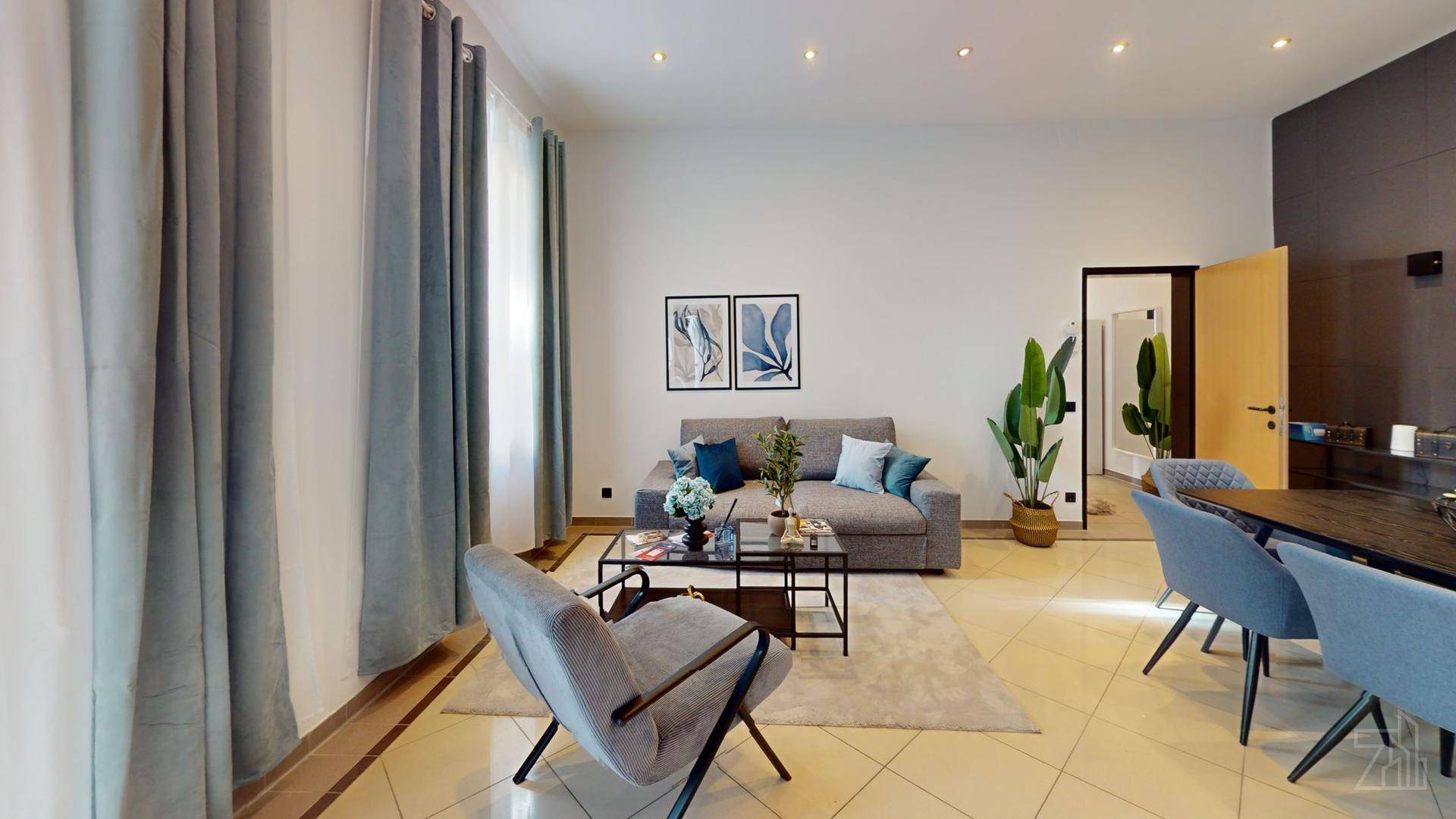 Gemütlicher Wohnbereich mit Sofa, Sessel und großen Fenstern, die viel Tageslicht hereinlassen.