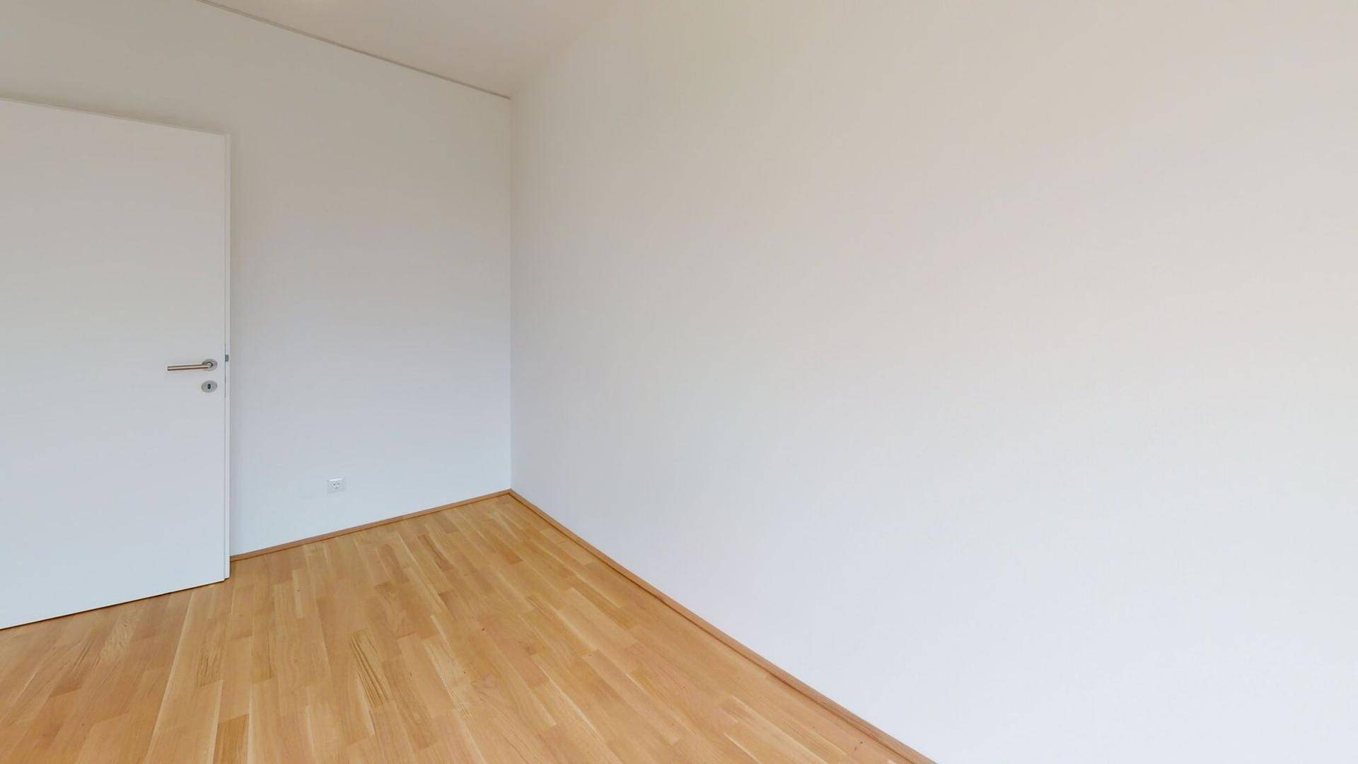 Leeres Zimmer mit hellem Parkettboden und weiß gestrichenen Wänden, bereit zur Einrichtung.