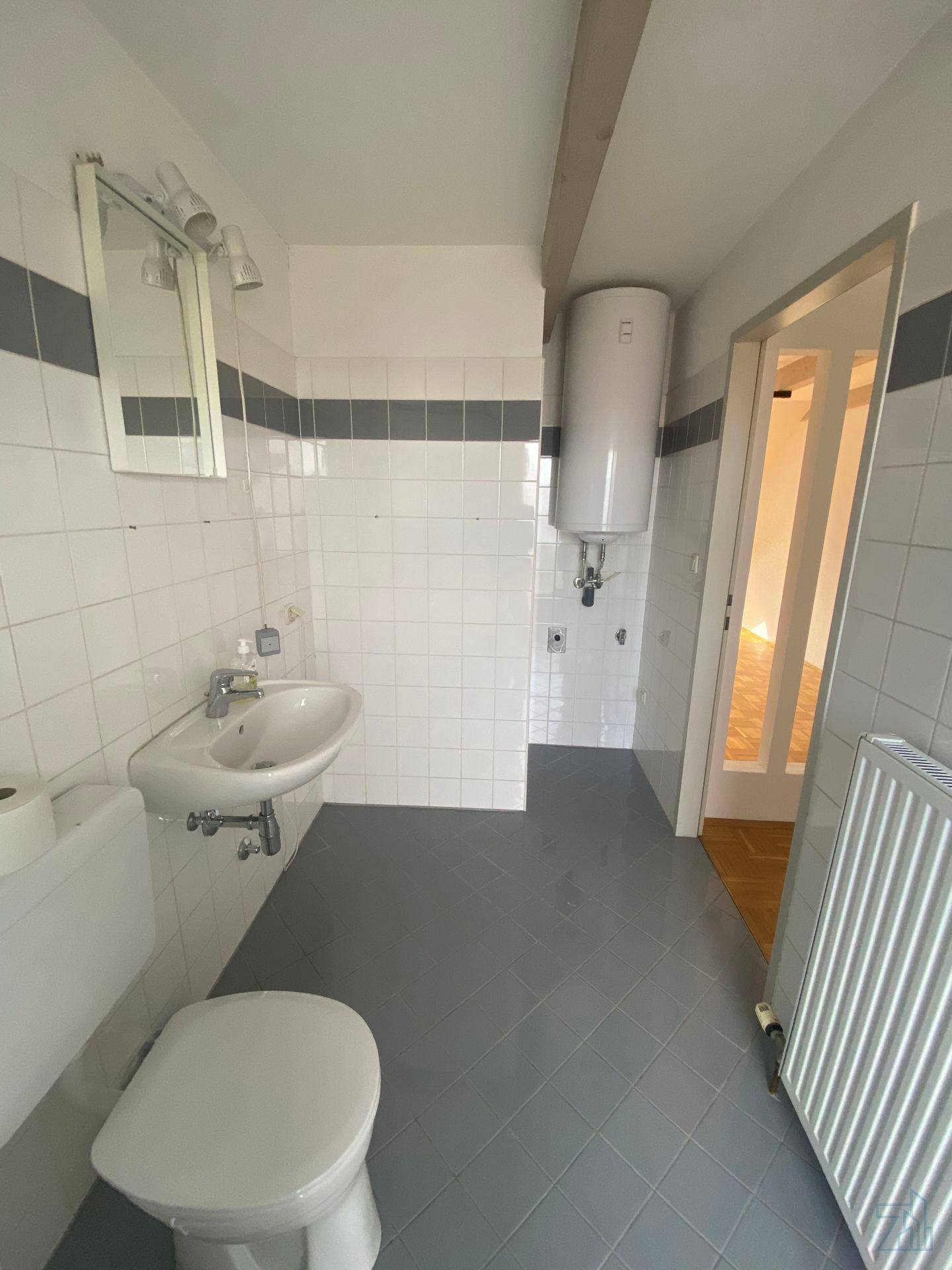 Badezimmer mit weißen Wandfliesen, grauen Bodenfliesen, Toilette und Waschbecken, funktional und sauber.