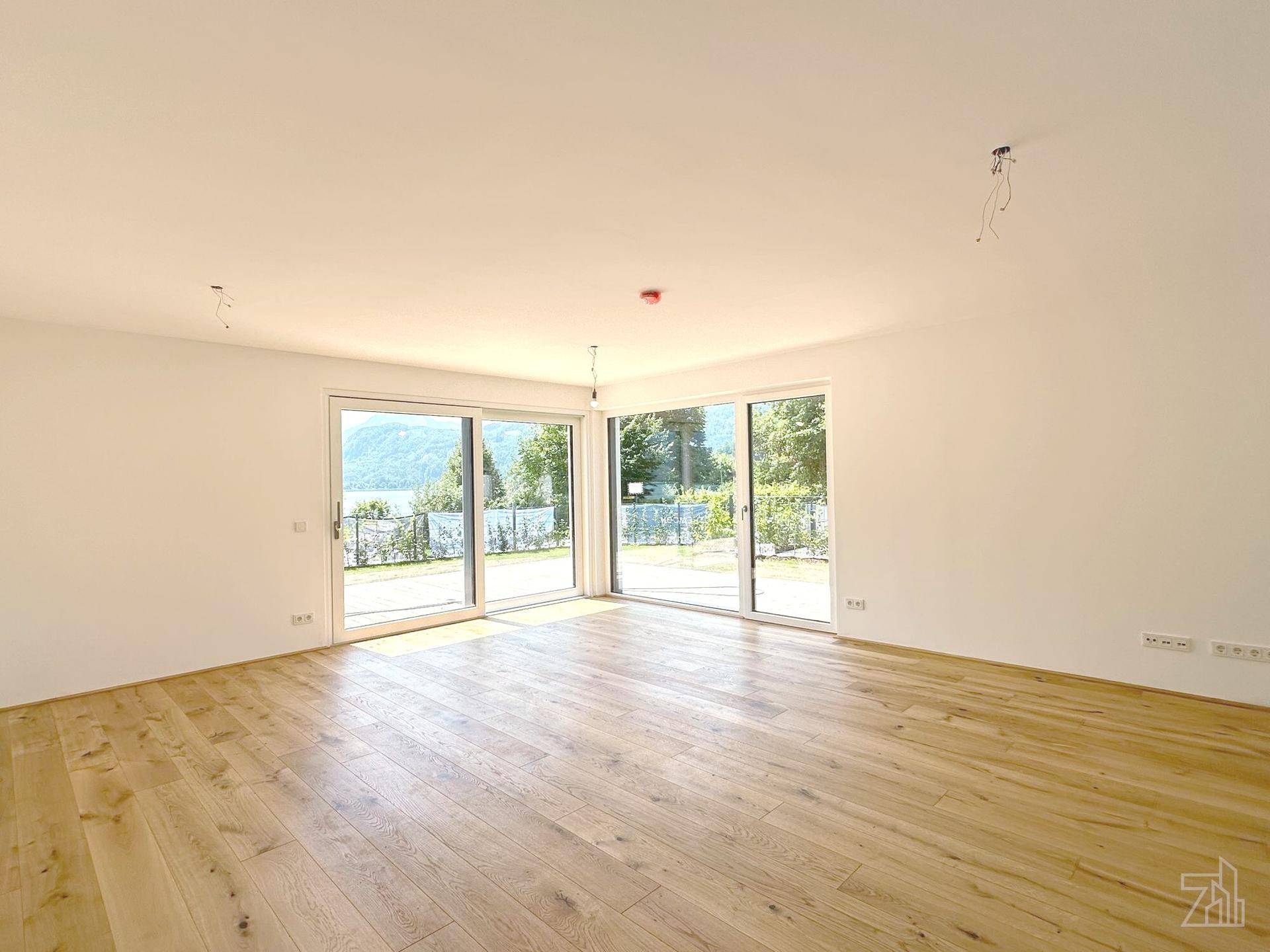 Heller Wohnraum mit Holzboden und großen Schiebetüren, die einen direkten Zugang zur Terrasse und Seeblick bieten.
