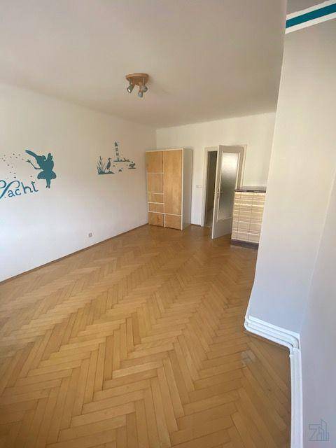 Leeres Zimmer mit Fischgrätparkettboden, hellen Wänden und einem Kleiderschrank.