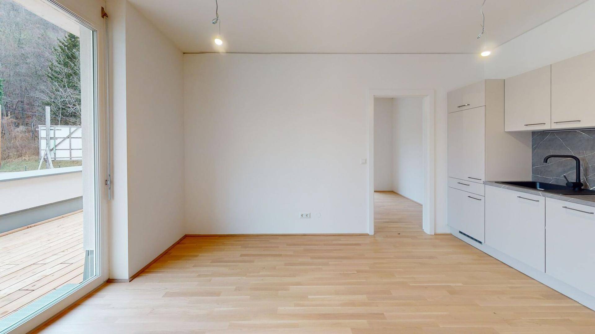 Heller Wohnbereich mit Holzboden, weißer Küchenzeile und Zugang zu einer Holzterrasse.