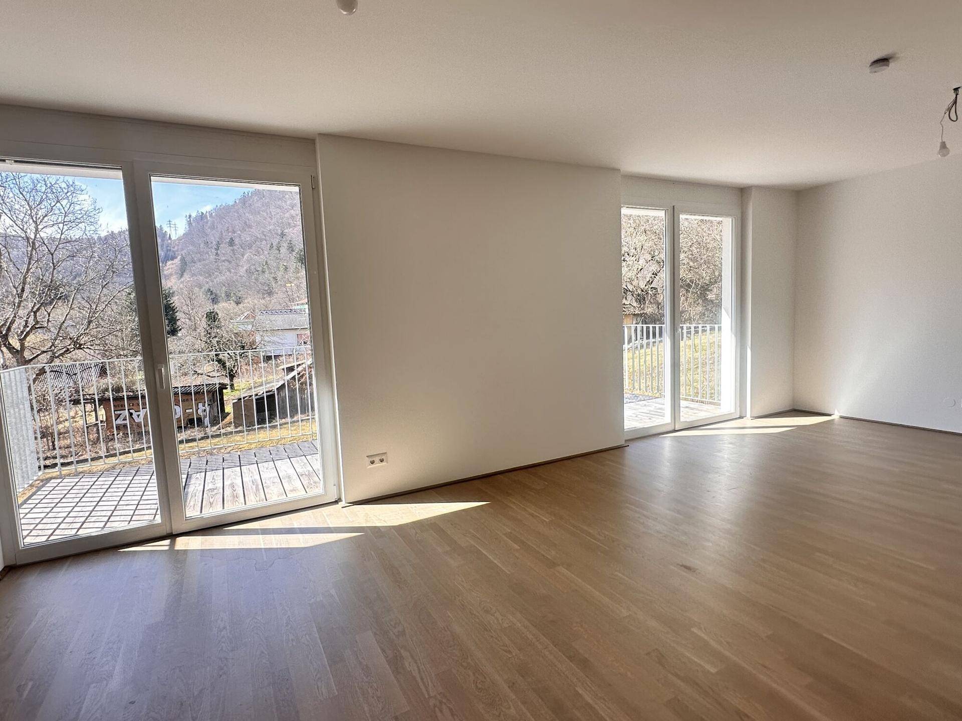 Helles Wohnzimmer mit Eichenparkett und Zugang zu einem Balkon mit Bergblick.