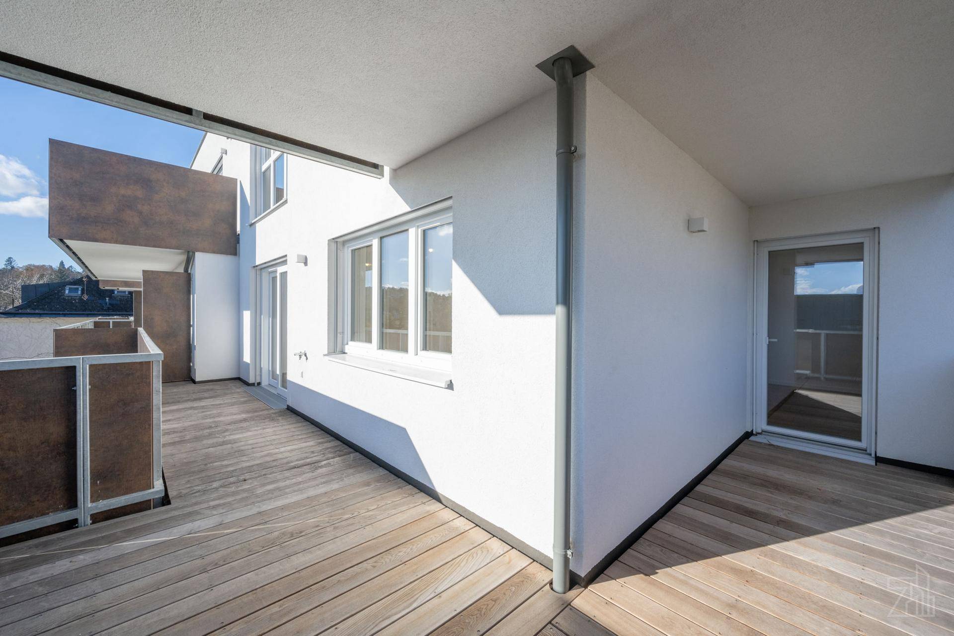 Geräumiger Balkon mit Holzboden und weißer Fassade, ideal für entspannte Stunden im Freien.