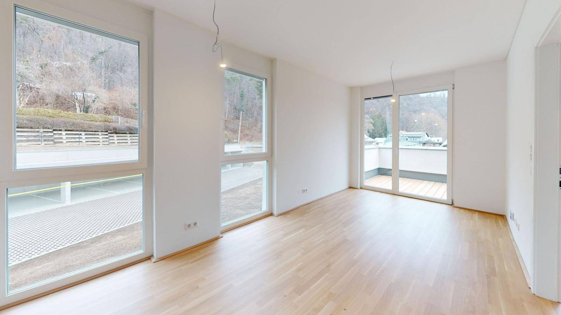 Geräumiges Wohnzimmer mit großen Fenstern, Holzboden und Zugang zum Balkon.