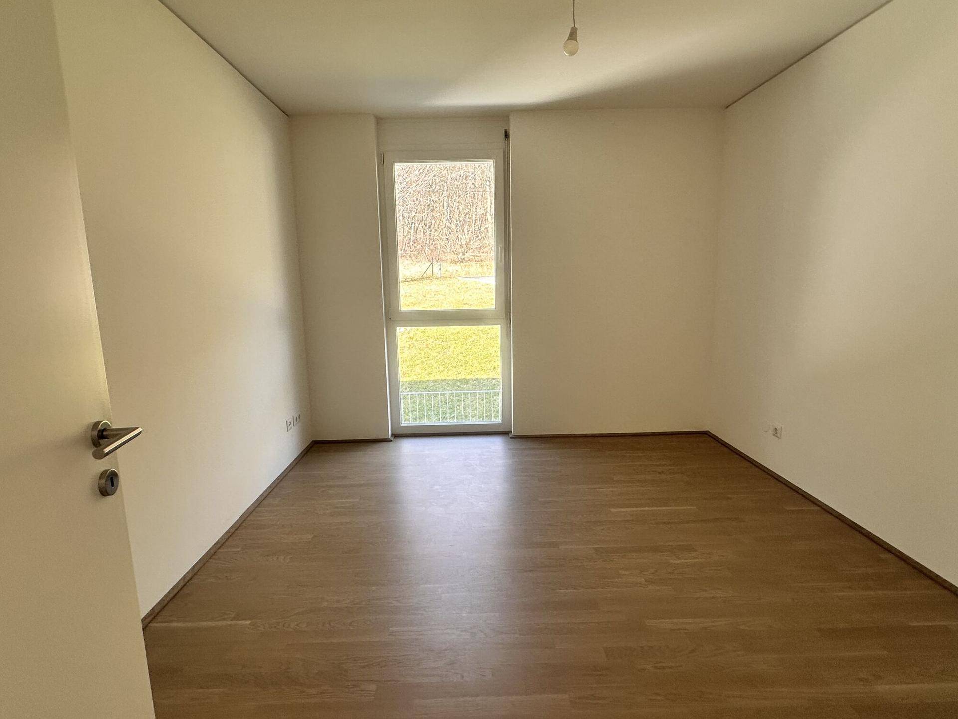 Helles Schlafzimmer mit Parkettboden und Fenster mit Blick ins Grüne.