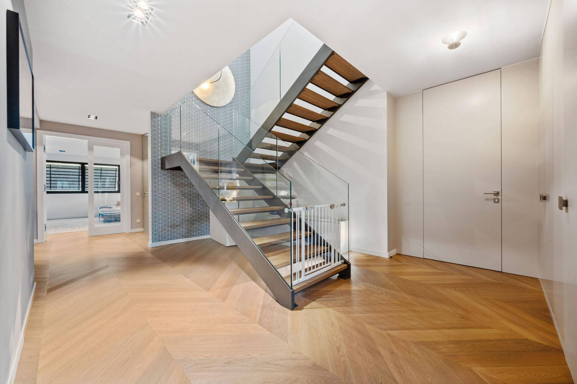 Moderner Flur mit Fischgrätparkett, eleganter Glastreppe und minimalistischem Design.