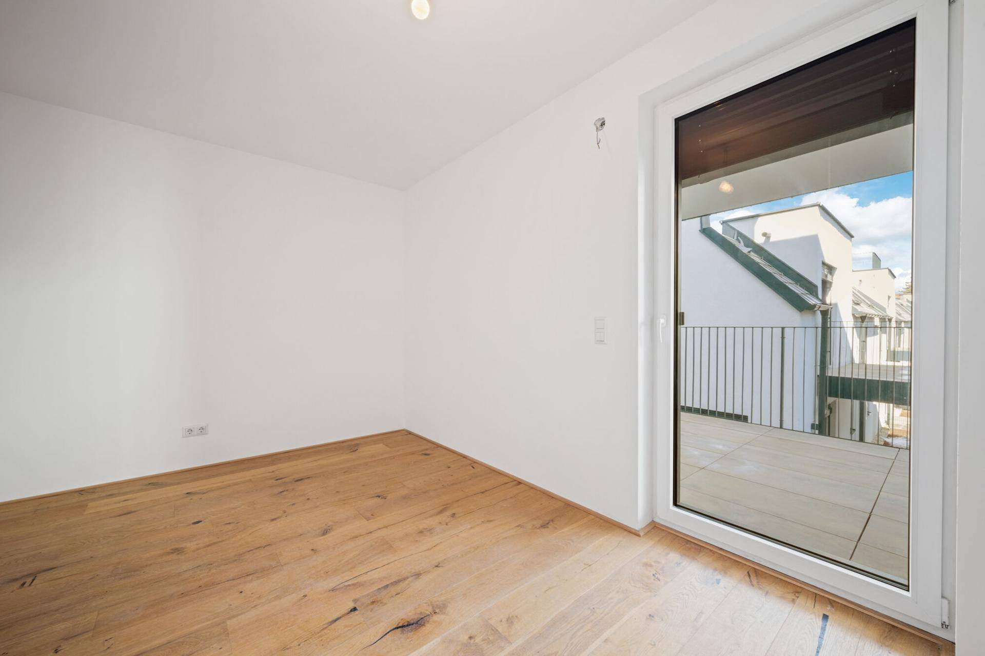 Leeres Schlafzimmer mit Holzdielenboden und direktem Zugang zu einem privaten Balkon.