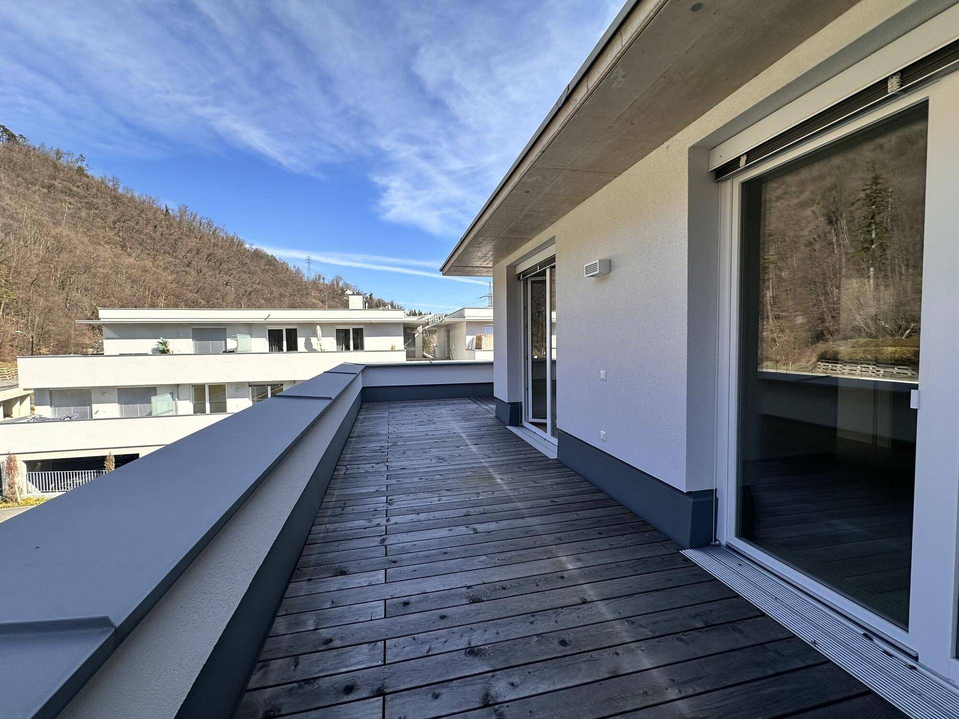 Weitläufige Dachterrasse mit Holzboden und moderner Glasbrüstung, sonnig und offen.