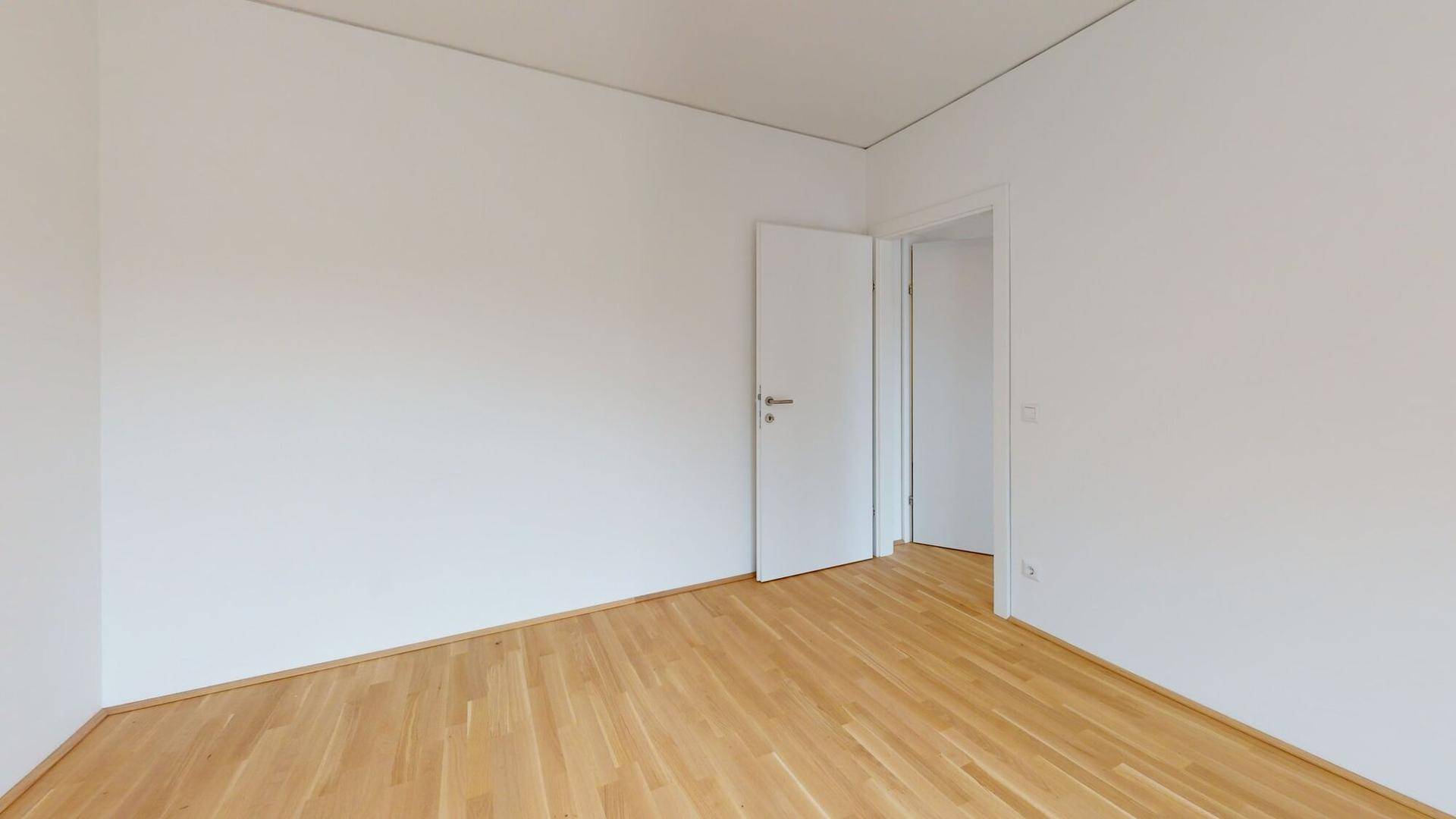 Heller, leerer Raum mit weiß gestrichenen Wänden und einem warmen Holzboden.
