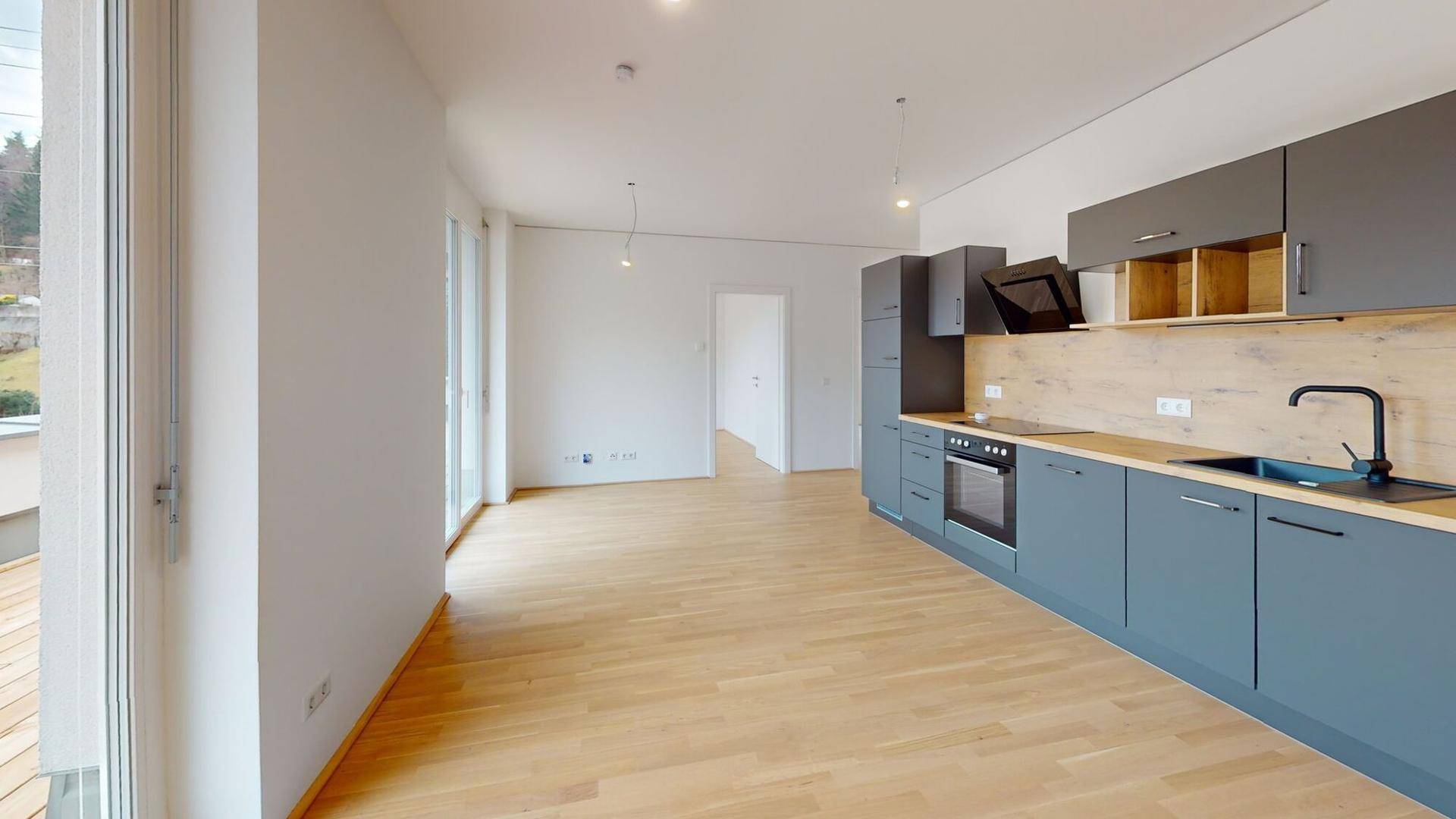 Offener Küchenbereich mit modernen grauen Schränken, Holzarbeitsplatte und Zugang zur Terrasse.